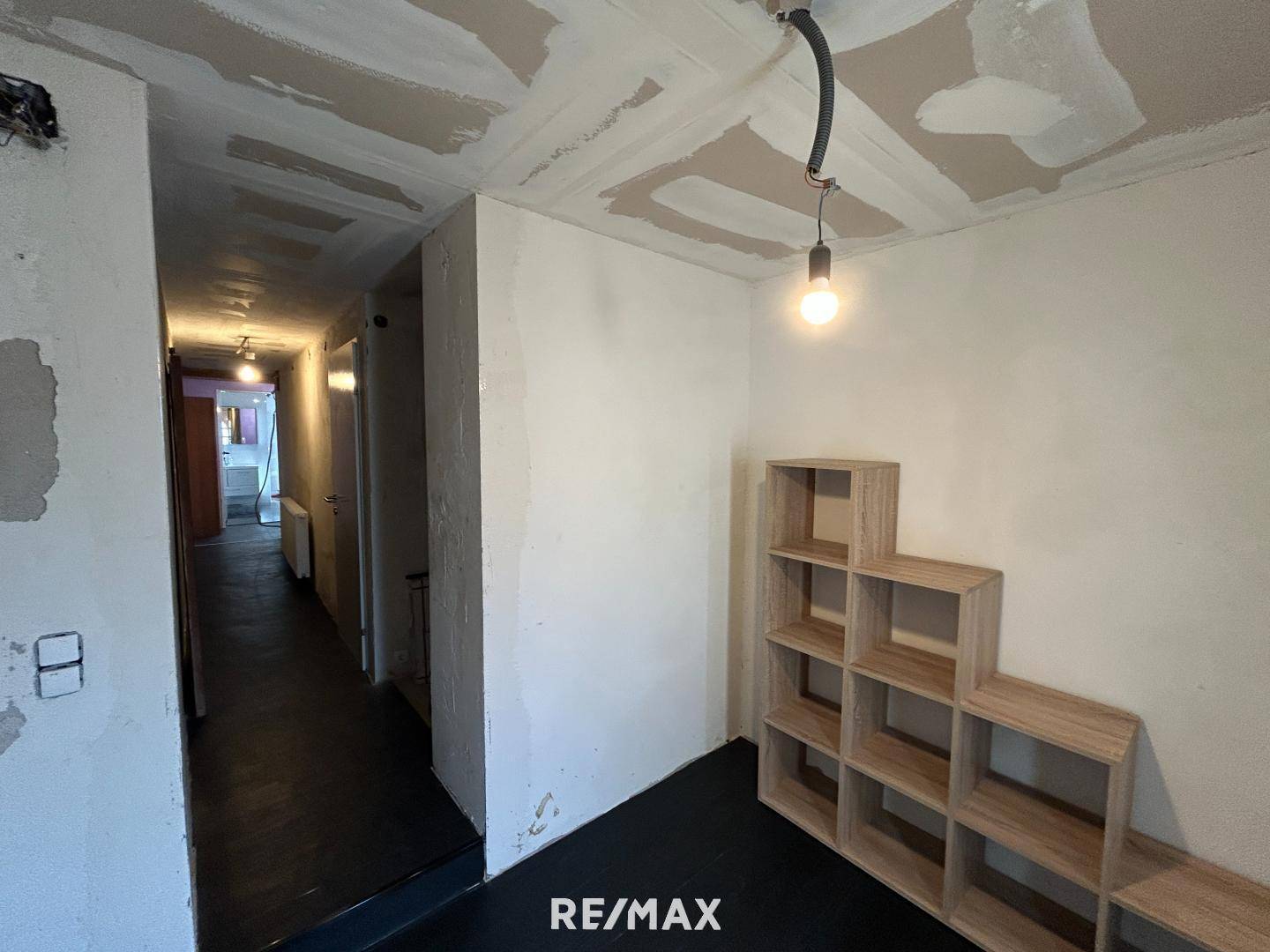 Flur mit Regalsystem und Blick in den renovierungsbedürftigen Gang.