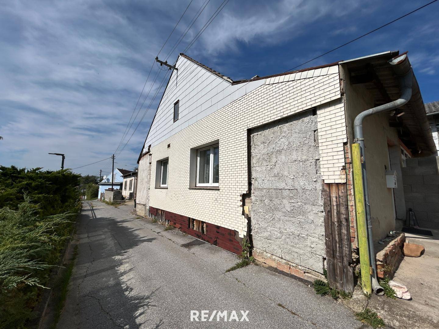 Seitenansicht eines älteren Gebäudes mit gemischter Fassade, die Renovierungsbedarf aufweist.