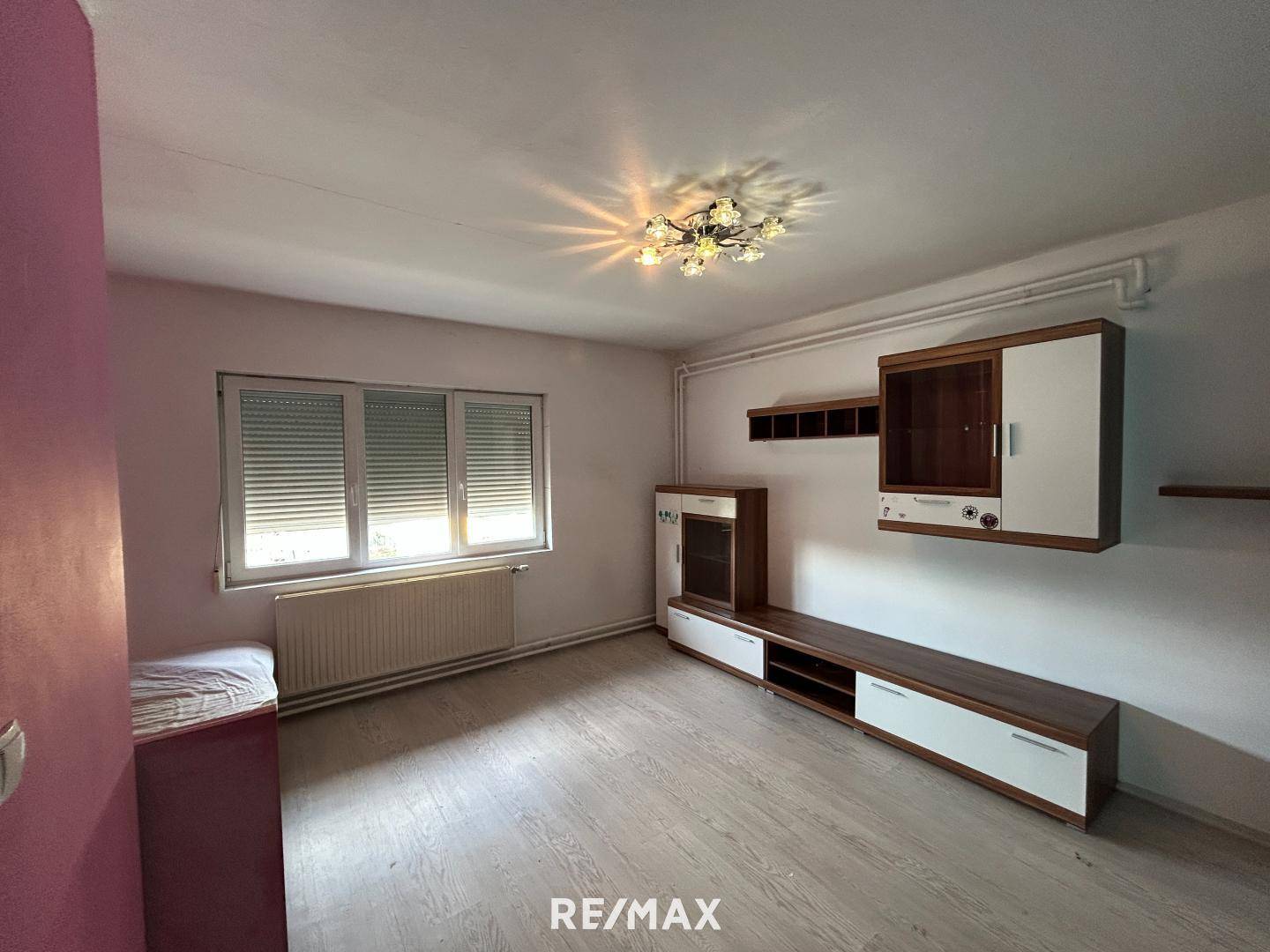 Wohnraum mit hellem Laminatboden, Fenster mit Rollläden und einer modernen Medienwand.