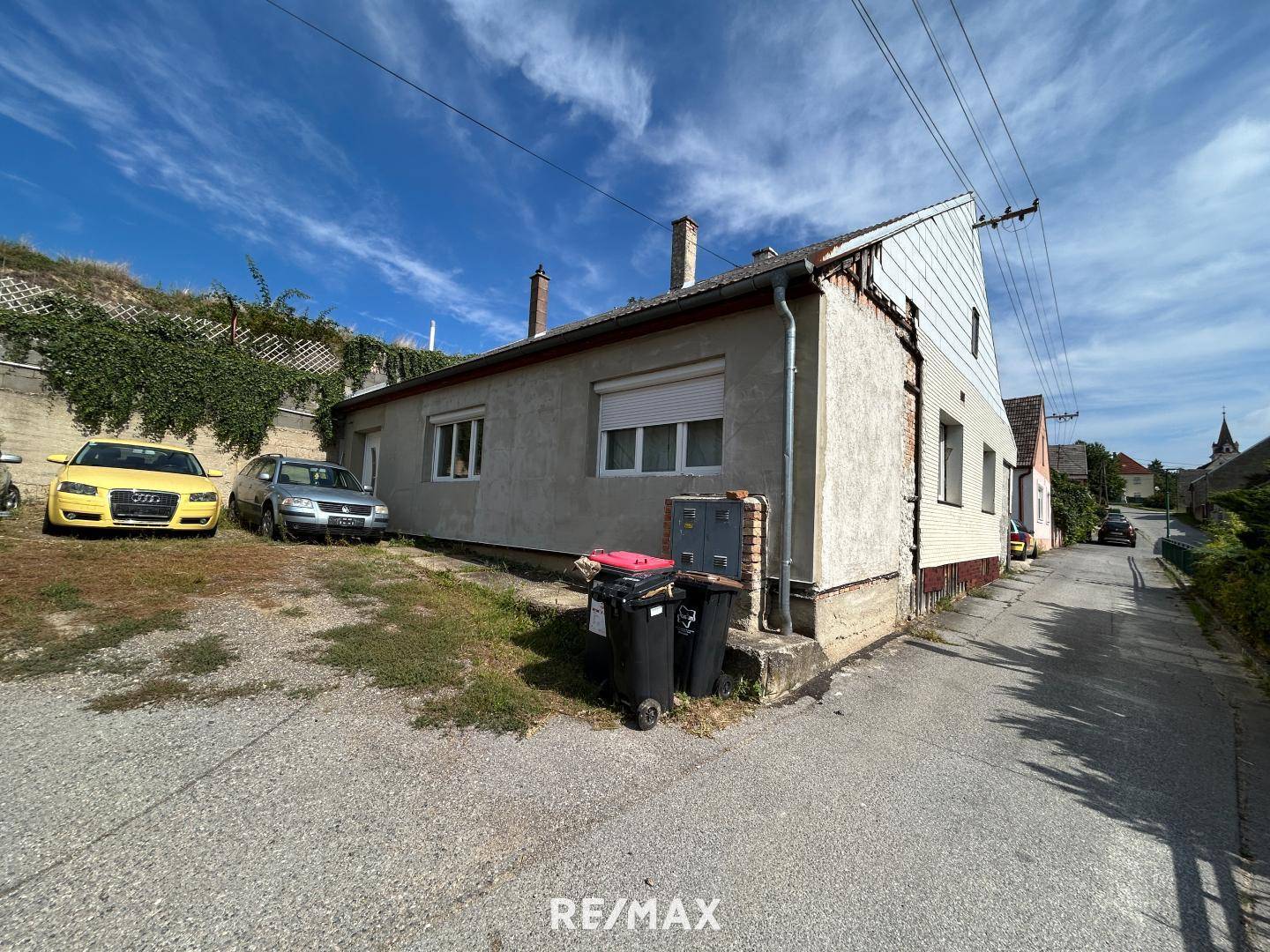 Seitenansicht eines älteren Hauses mit Parkplatz und sichtbaren Abnutzungserscheinungen.