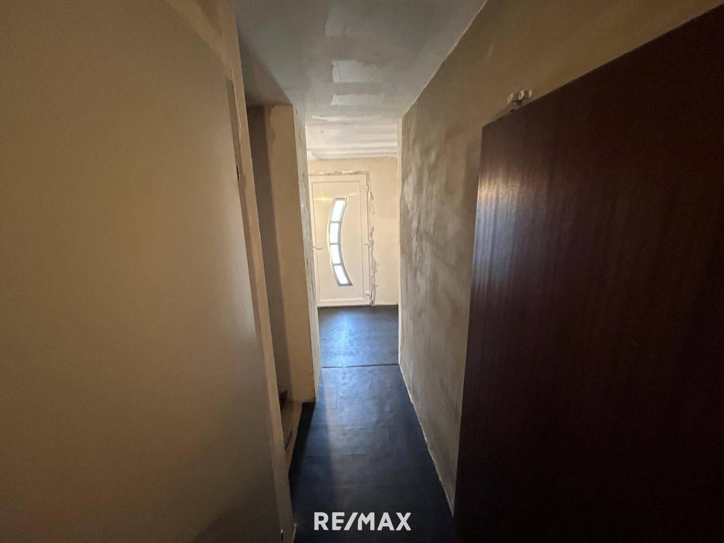 Flur im Renovierungszustand mit unfertigen Wänden und dunklem Bodenbelag.