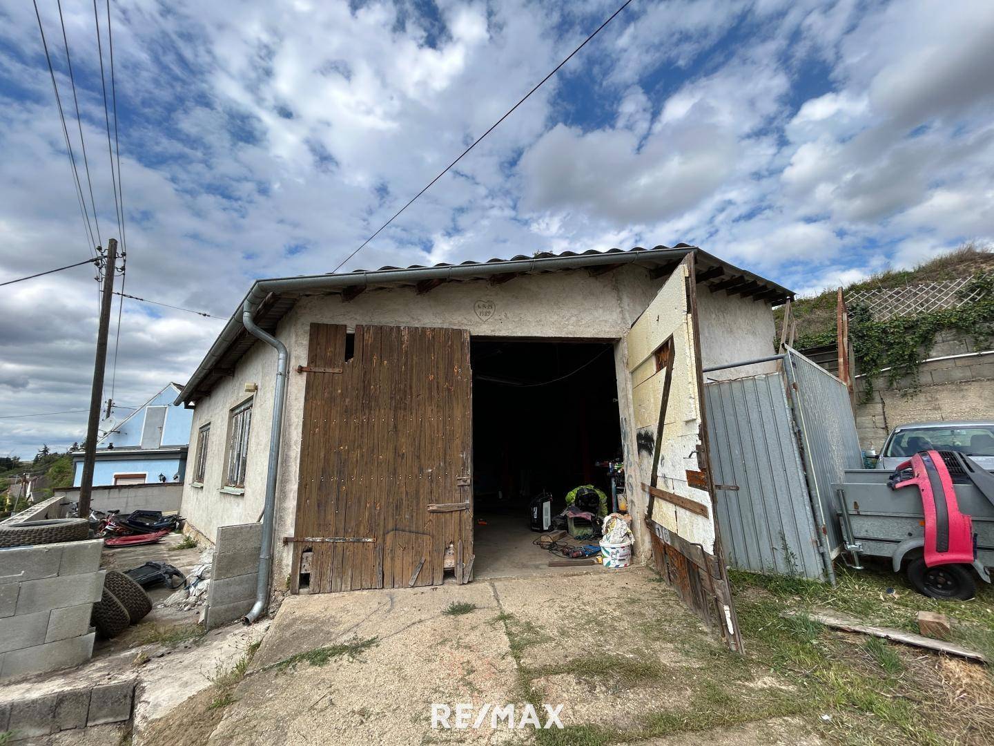 Außenseite der Garage mit Holztoren und Zufahrt, die Renovierungsbedarf aufweist.
