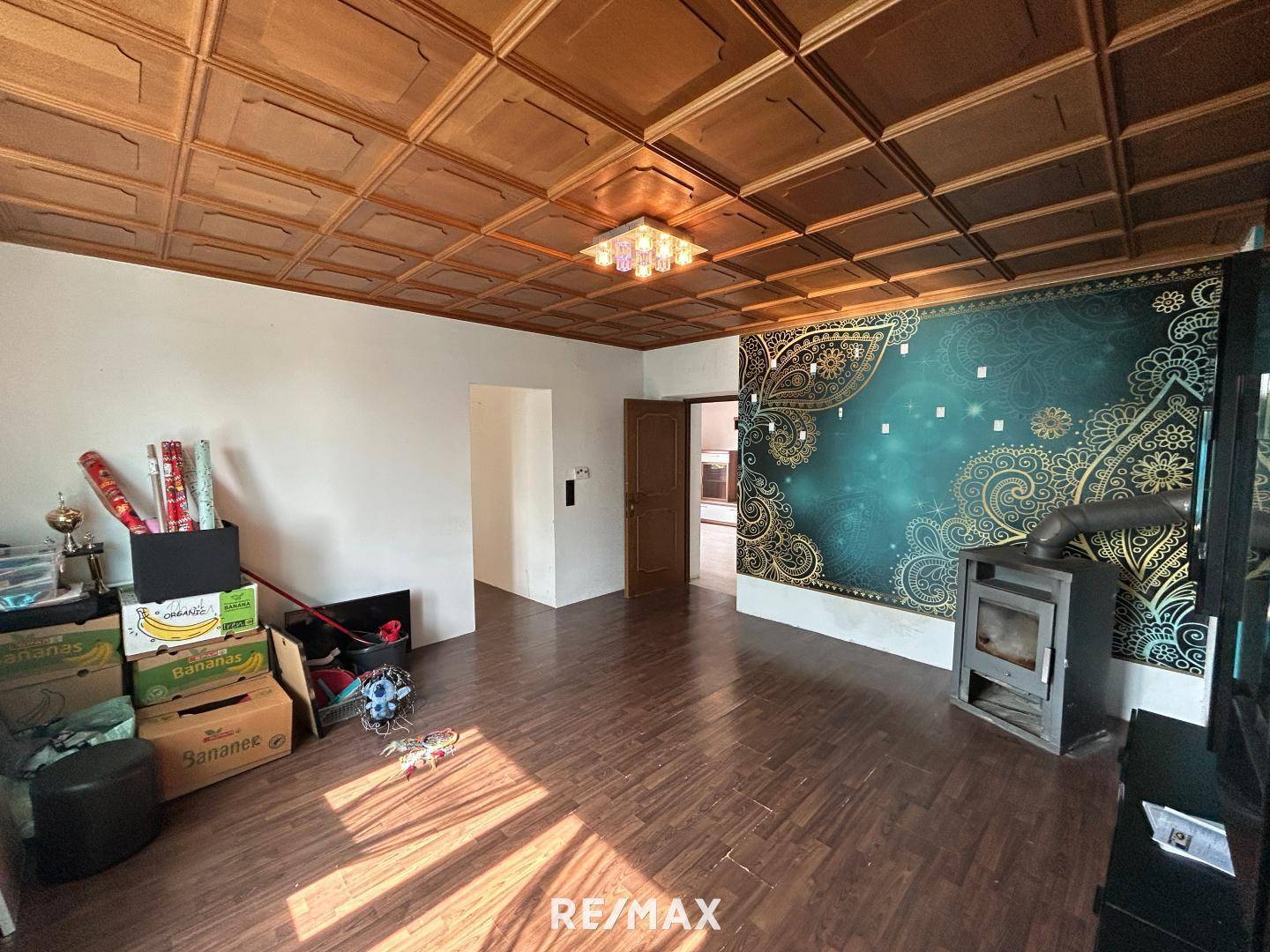 Wohnzimmer mit Holzkassettendecke, dekorativer Tapete und einem gemütlichen Holzofen.