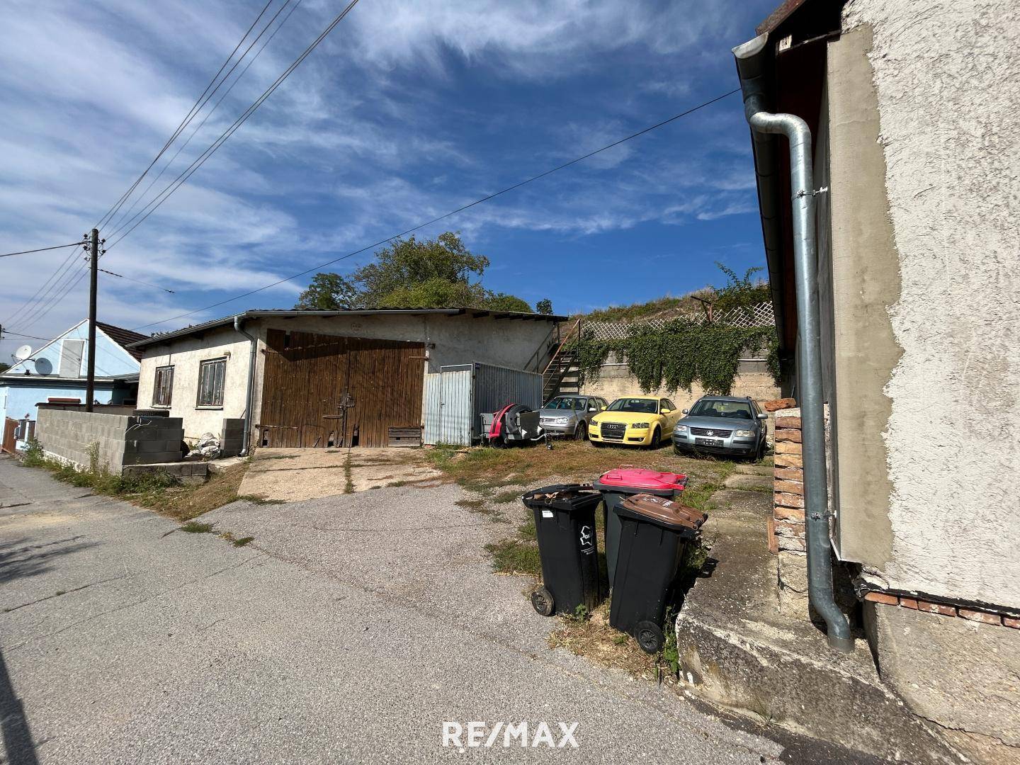 Außenbereich mit Parkplätzen und einem älteren Garagengebäude unter blauem Himmel.