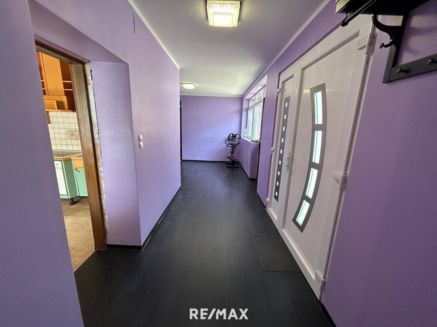Langer Flur mit lila Wänden, dunklem Boden und einer weißen Eingangstür.