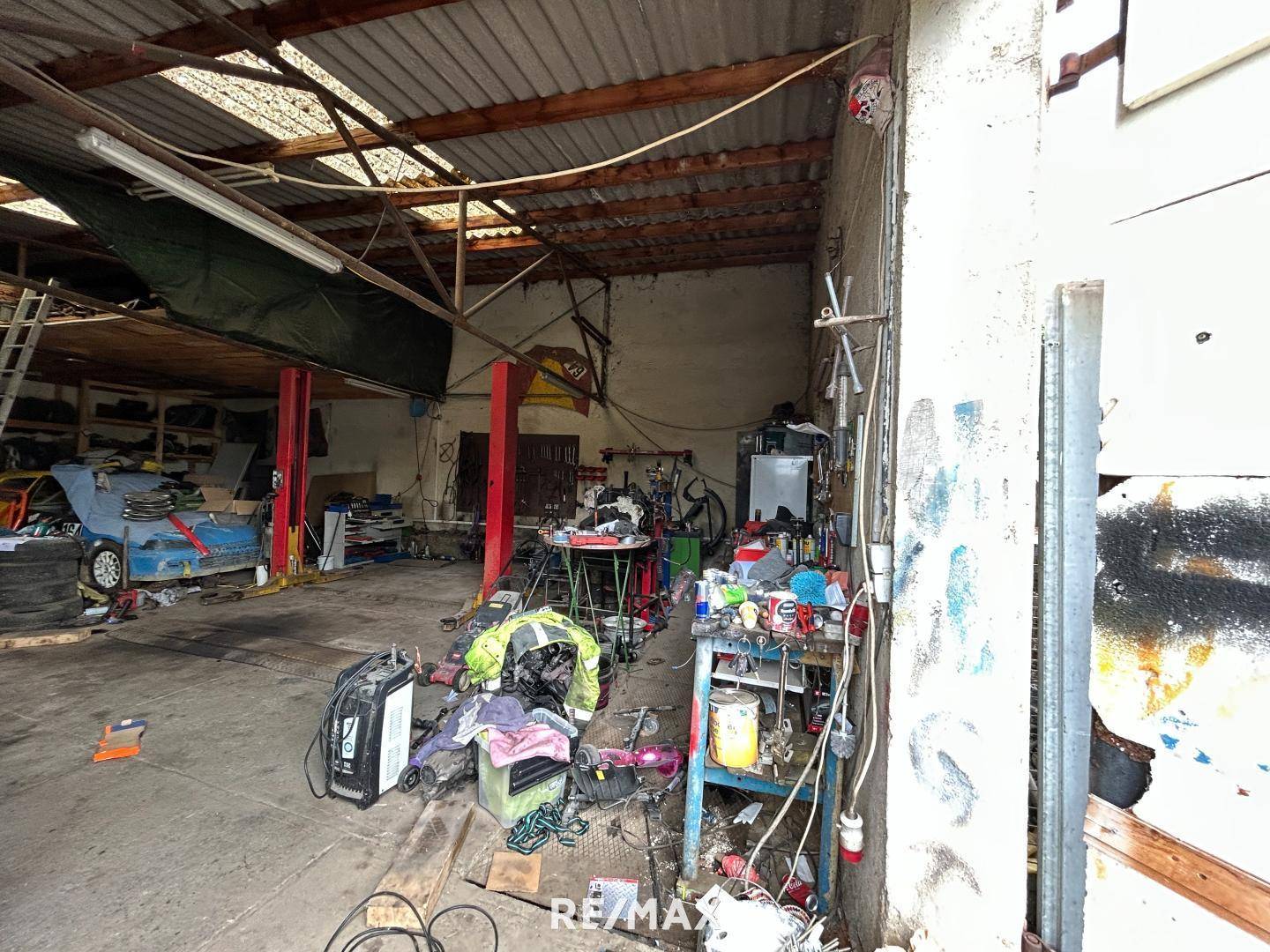 Geräumige Garage oder Werkstatt mit Werkzeugen und Fahrzeugteilen, die Renovierung benötigt.