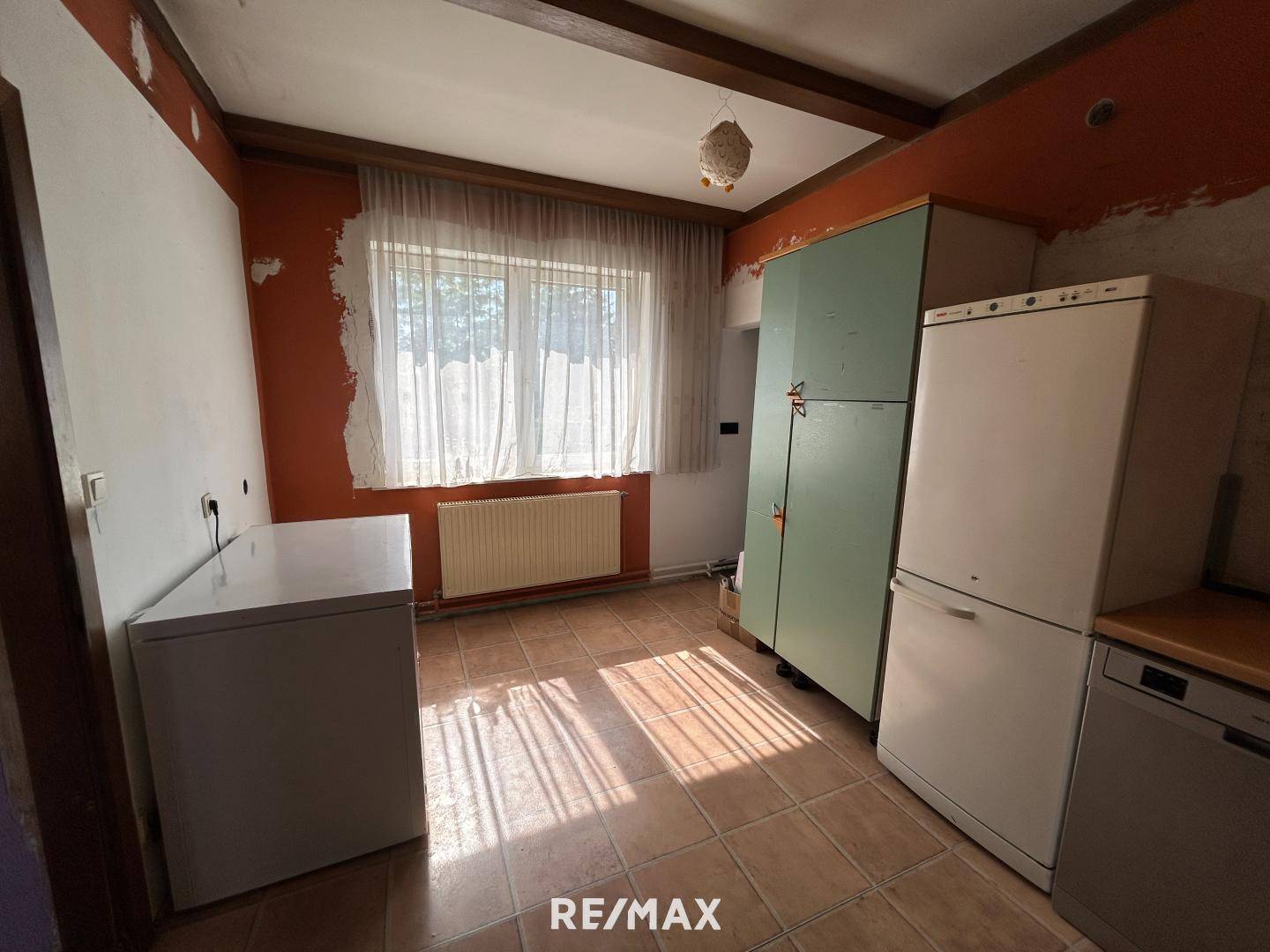 Küche mit Fliesenboden, Fenster und vorhandenen Geräten, die Renovierung benötigt.