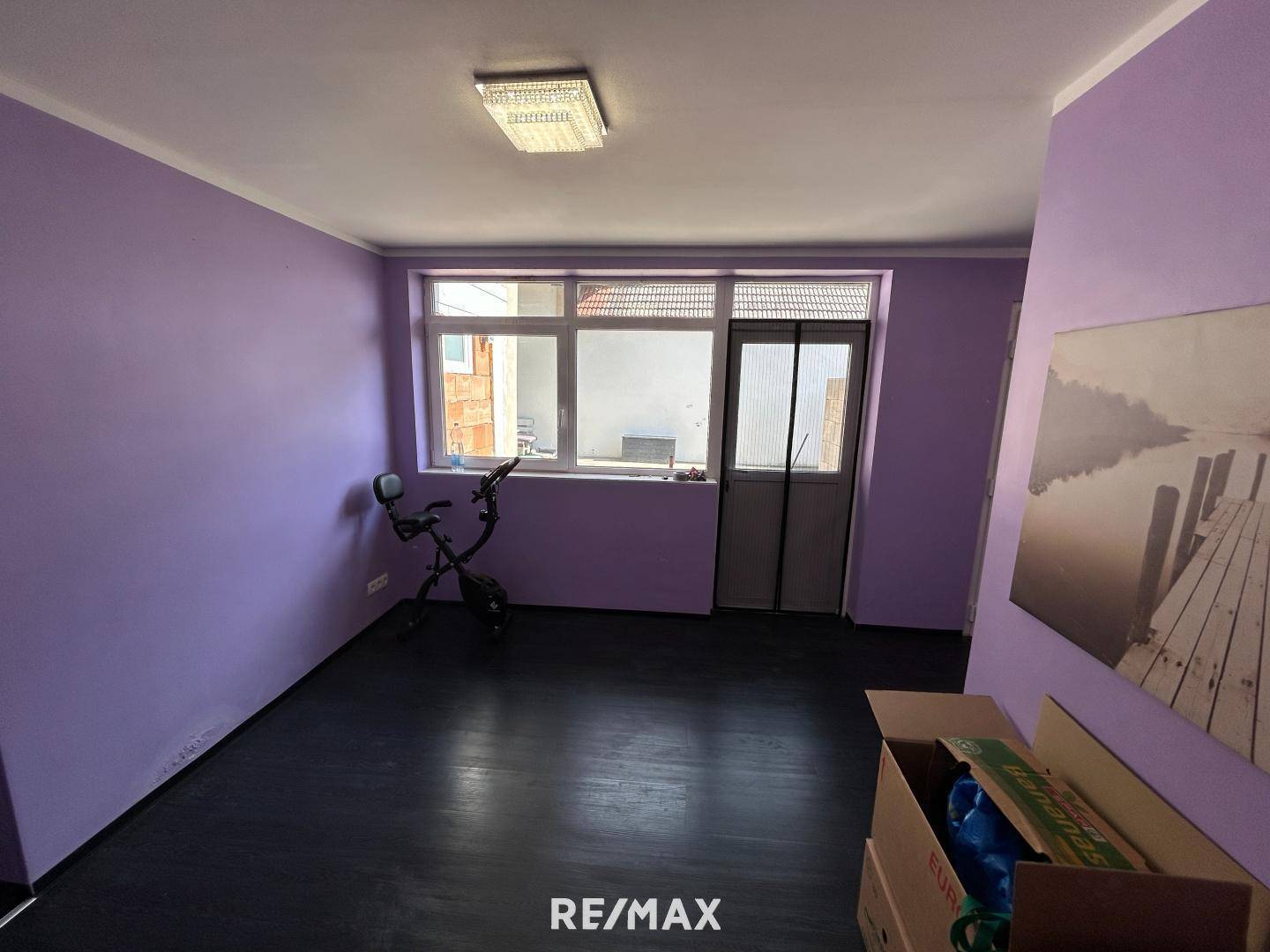 Raum mit lila Wänden, dunklem Boden und einer Tür, die ins Freie führt, mit viel Tageslicht.