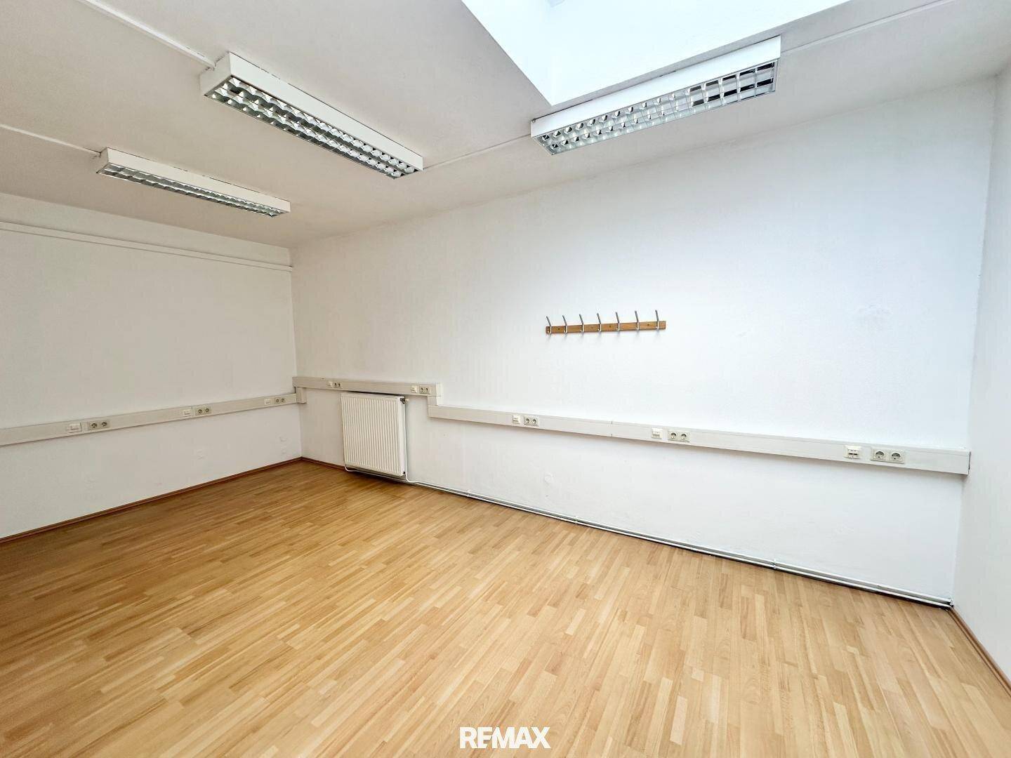 Heller Büroraum mit Holzparkettboden, weißen Wänden und praktischer Garderobe, ideal für Arbeitszwecke.