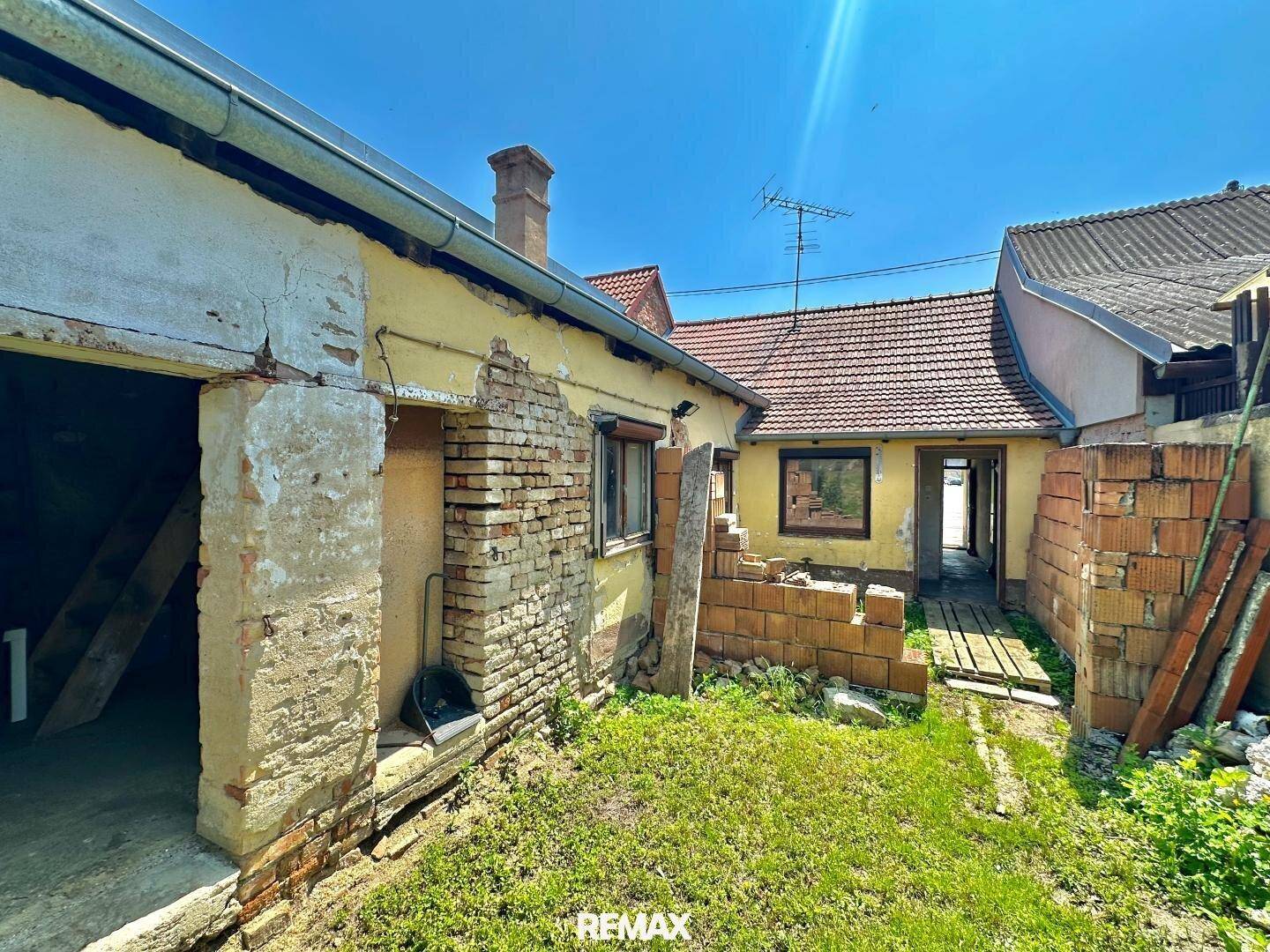 Rückansicht des Hauses mit sichtbaren Bauschäden, freiliegenden Ziegeln und einem Schornstein.