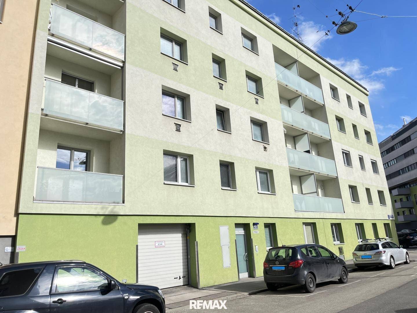 Mehrstöckiges Wohngebäude mit hellgrüner Fassade, Balkonen und einer Garage im Erdgeschoss.
