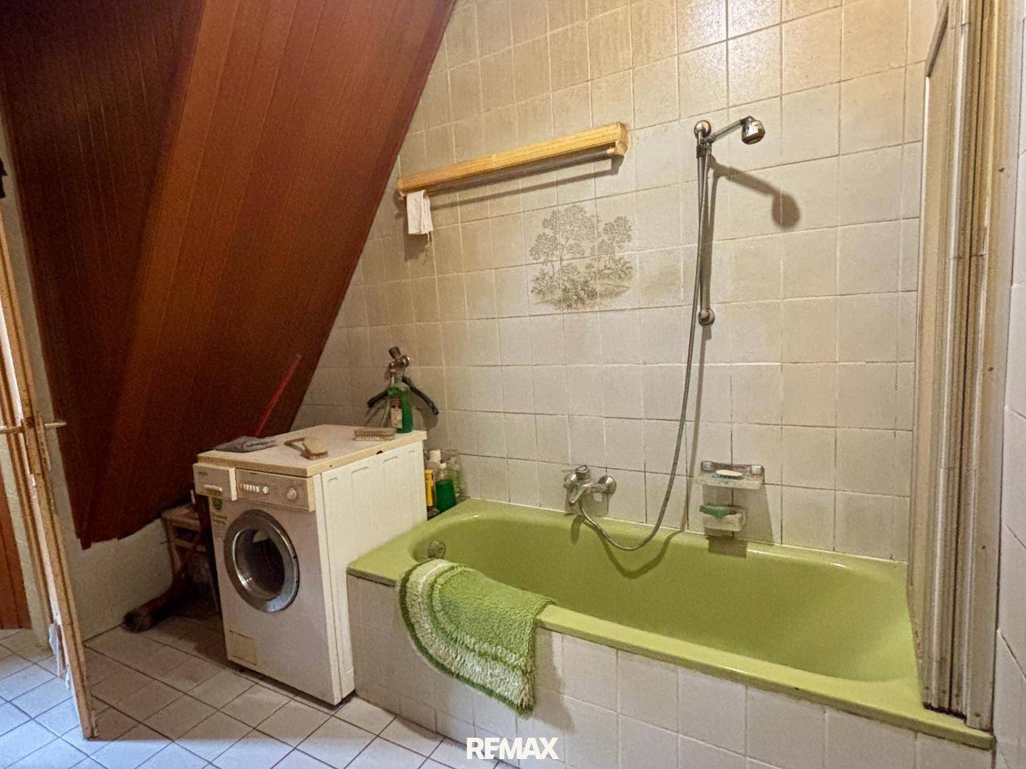 Badezimmer mit grüner Badewanne, Fliesen und Waschmaschine, das eine Modernisierung erfordert.