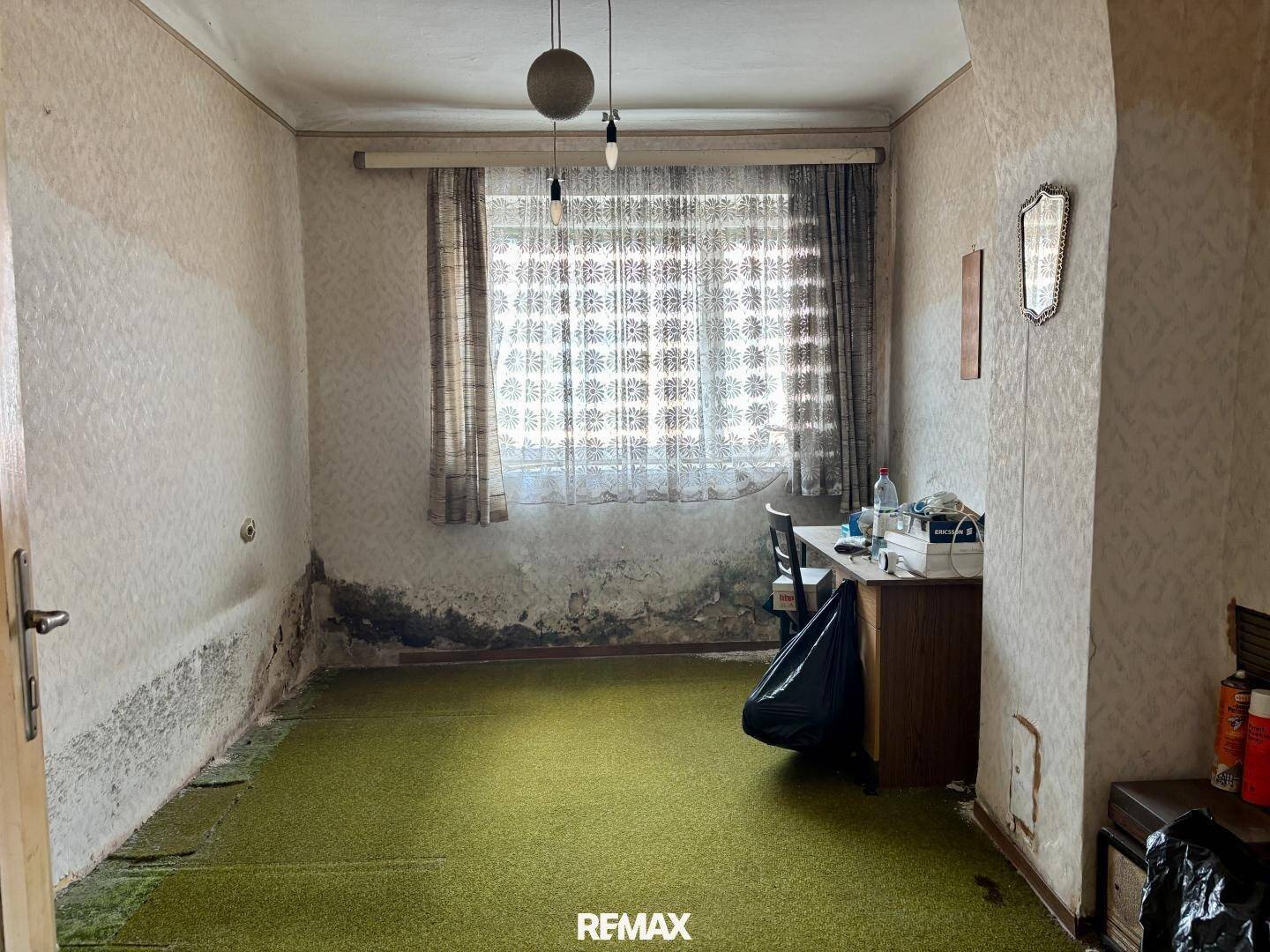 Schlafzimmer mit grünem Teppichboden, abgenutzten Wänden und einem Fenster, das Renovierung benötigt.