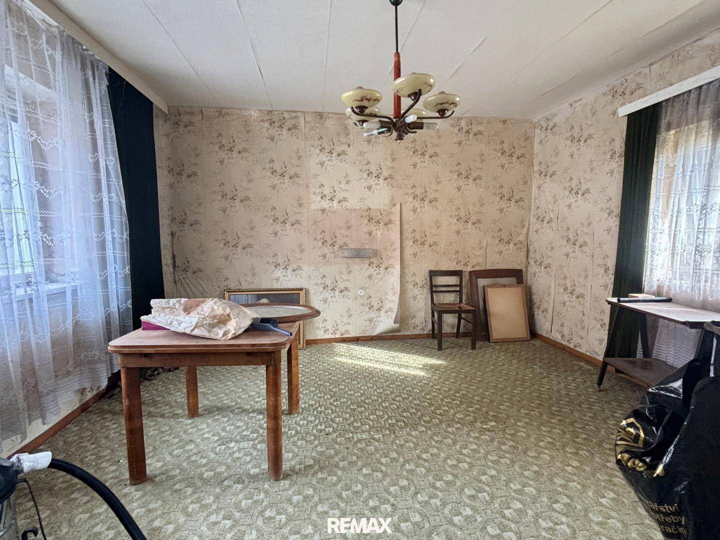 Wohnzimmer mit Teppichboden, floraler Tapete und einem Holztisch, das eine Renovierung erfordert.