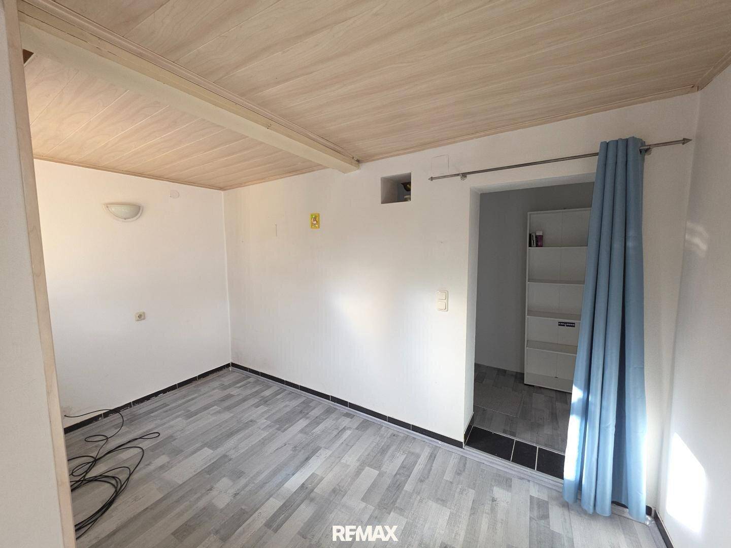 Raum mit hellem Holzboden, weißen Wänden und sichtbaren Kabeln, möglicherweise ein Abstellraum.