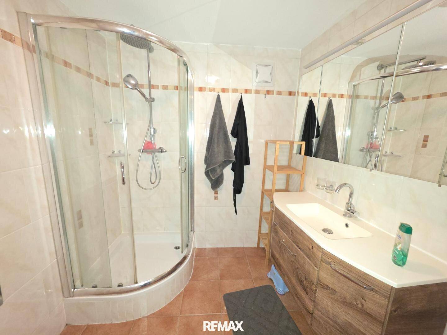 Helles Badezimmer mit Duschkabine, Waschbeckenunterschrank und großen Wandfliesen.
