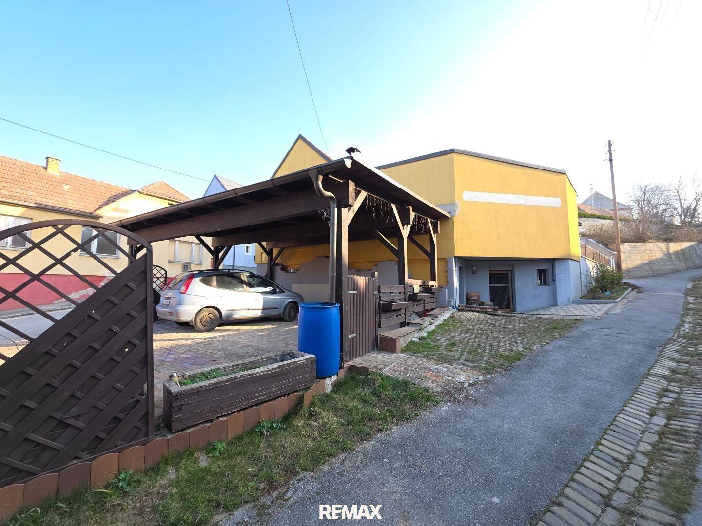 Überdachter Stellplatz neben dem Haus mit gelber Fassade und Blick auf die Umgebung.