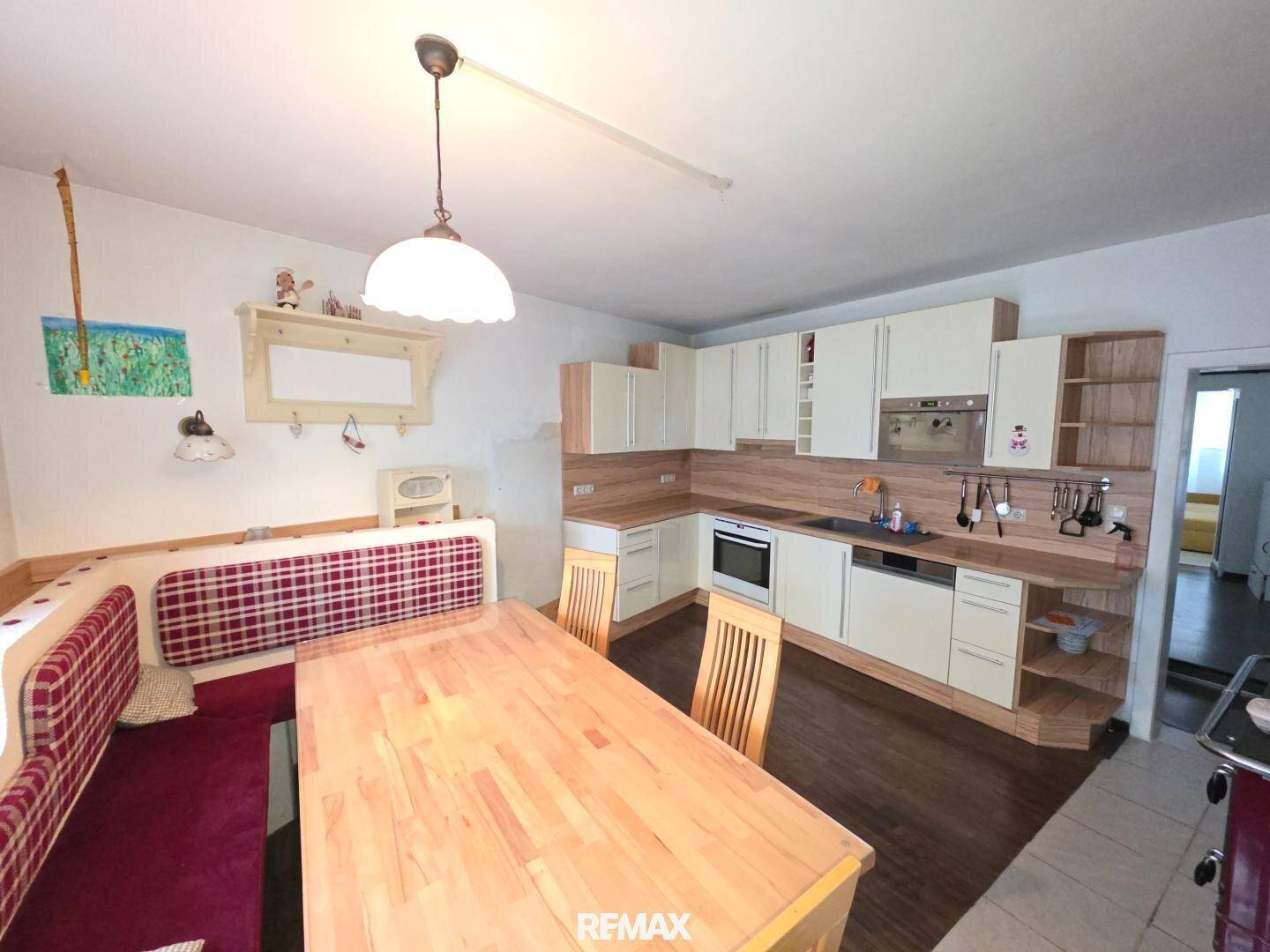 Gemütliche Wohnküche mit Holztisch, Eckbank und Einbauküche in hellem Holzton.