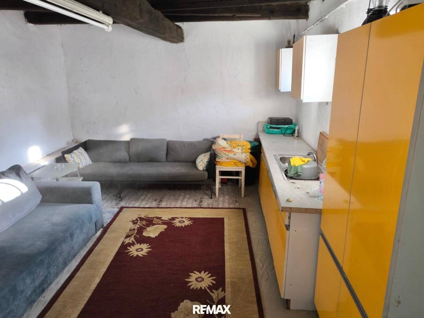 Rustikaler Wohnraum mit freiliegenden Holzbalken, gelber Küchenzeile und gemütlichem Sofa.