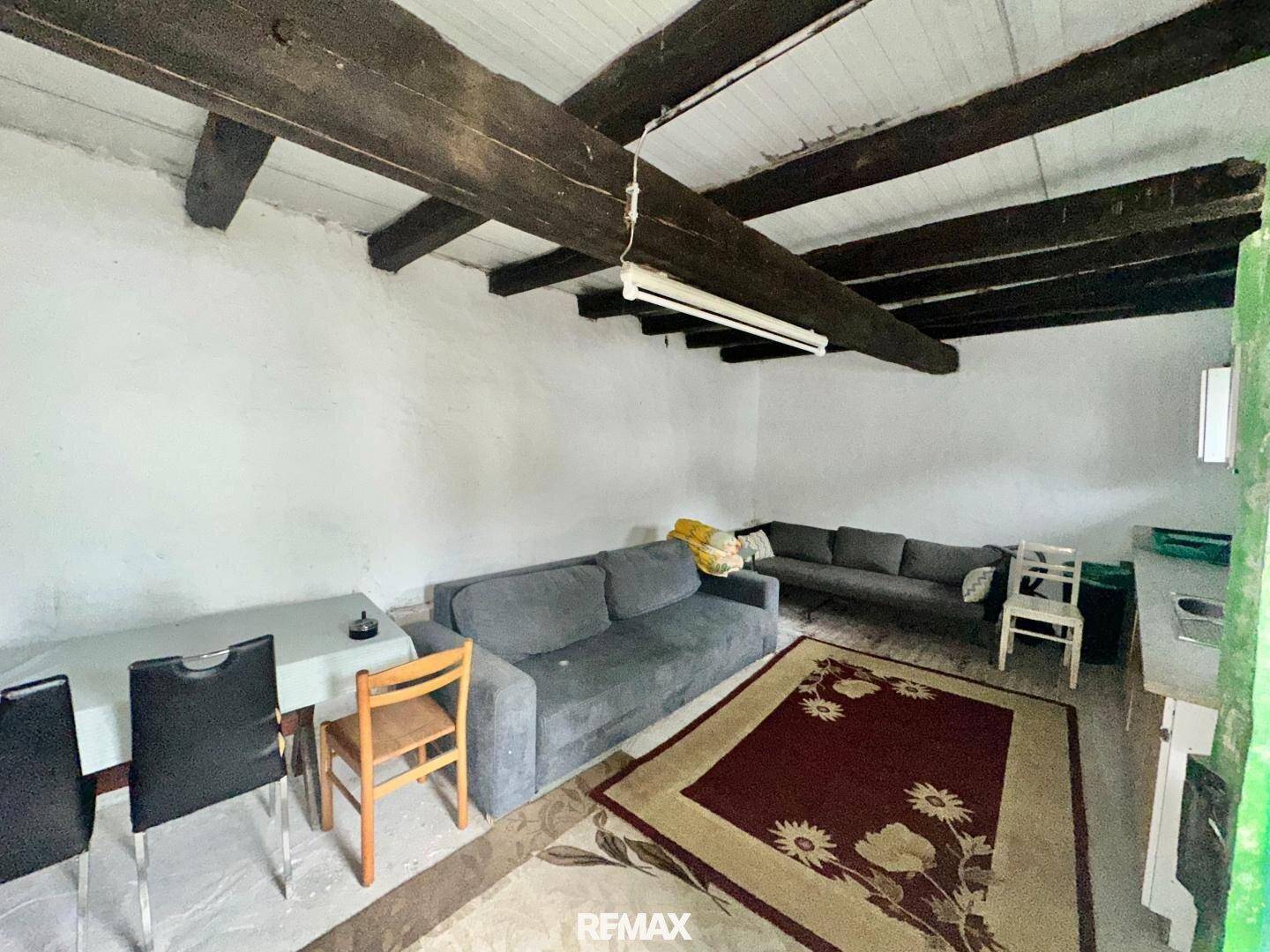 Heller Wohnraum mit zwei Sofas, einem Esstisch und rustikalen Holzbalken an der Decke.
