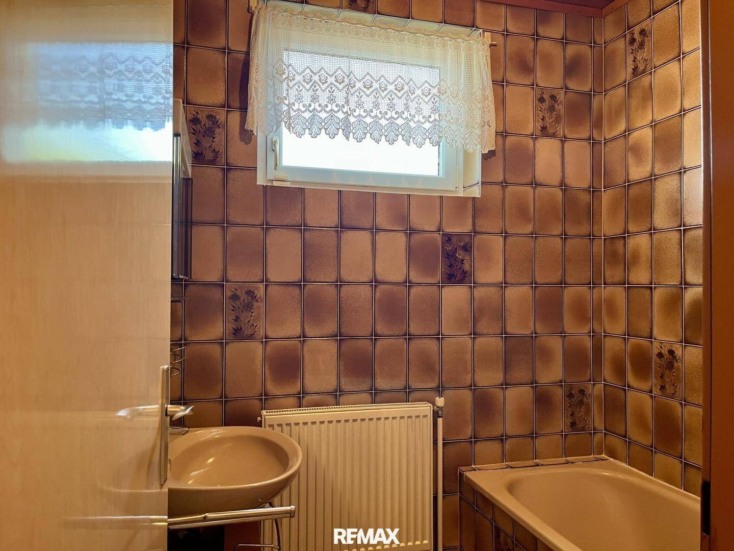 Badezimmer im 80er-Jahre-Stil mit braunen Fliesen, Badewanne und Fenster.