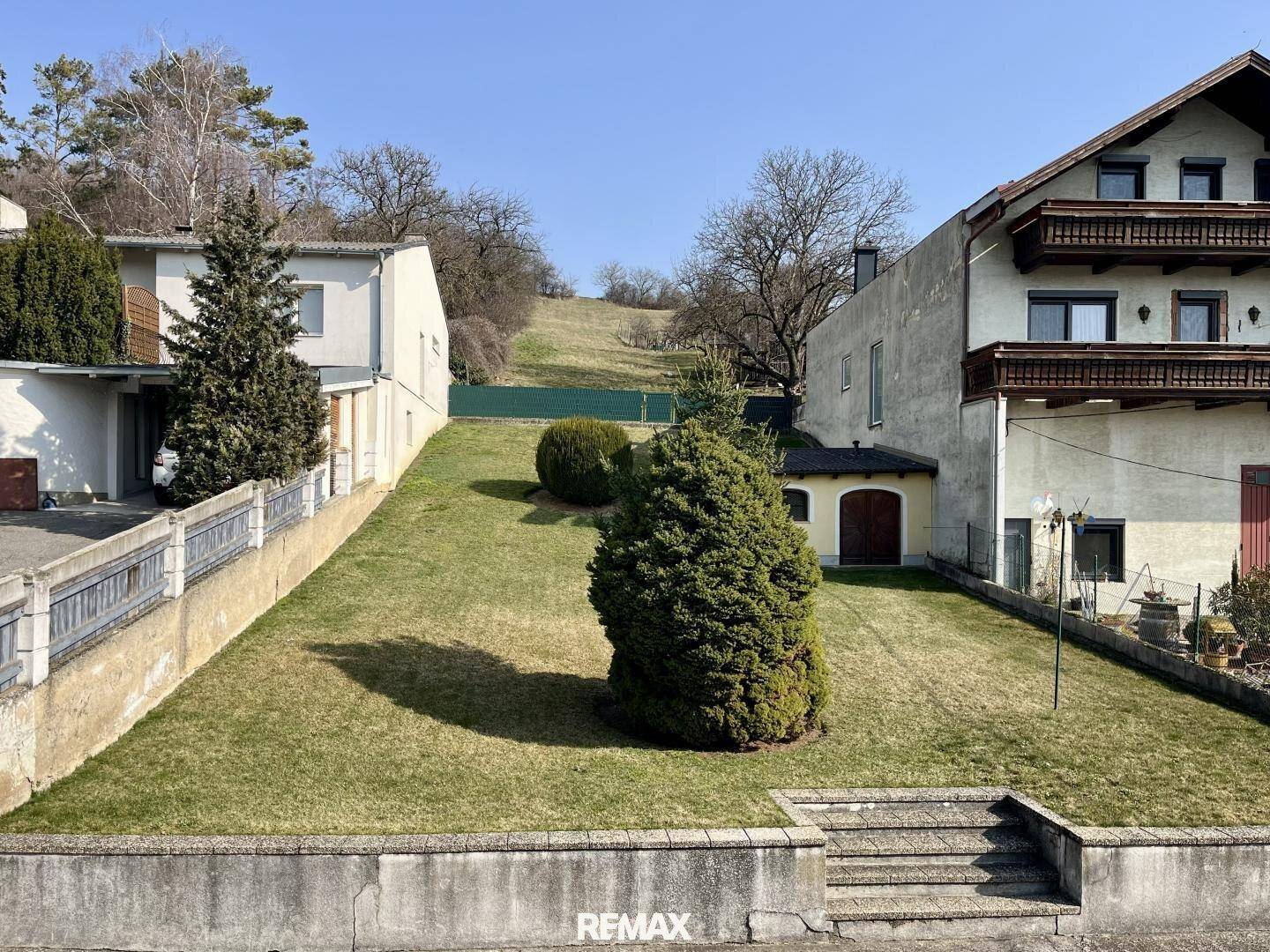 Großer Garten mit Rasenfläche und Bäumen, eingebettet in eine grüne Hügellandschaft.