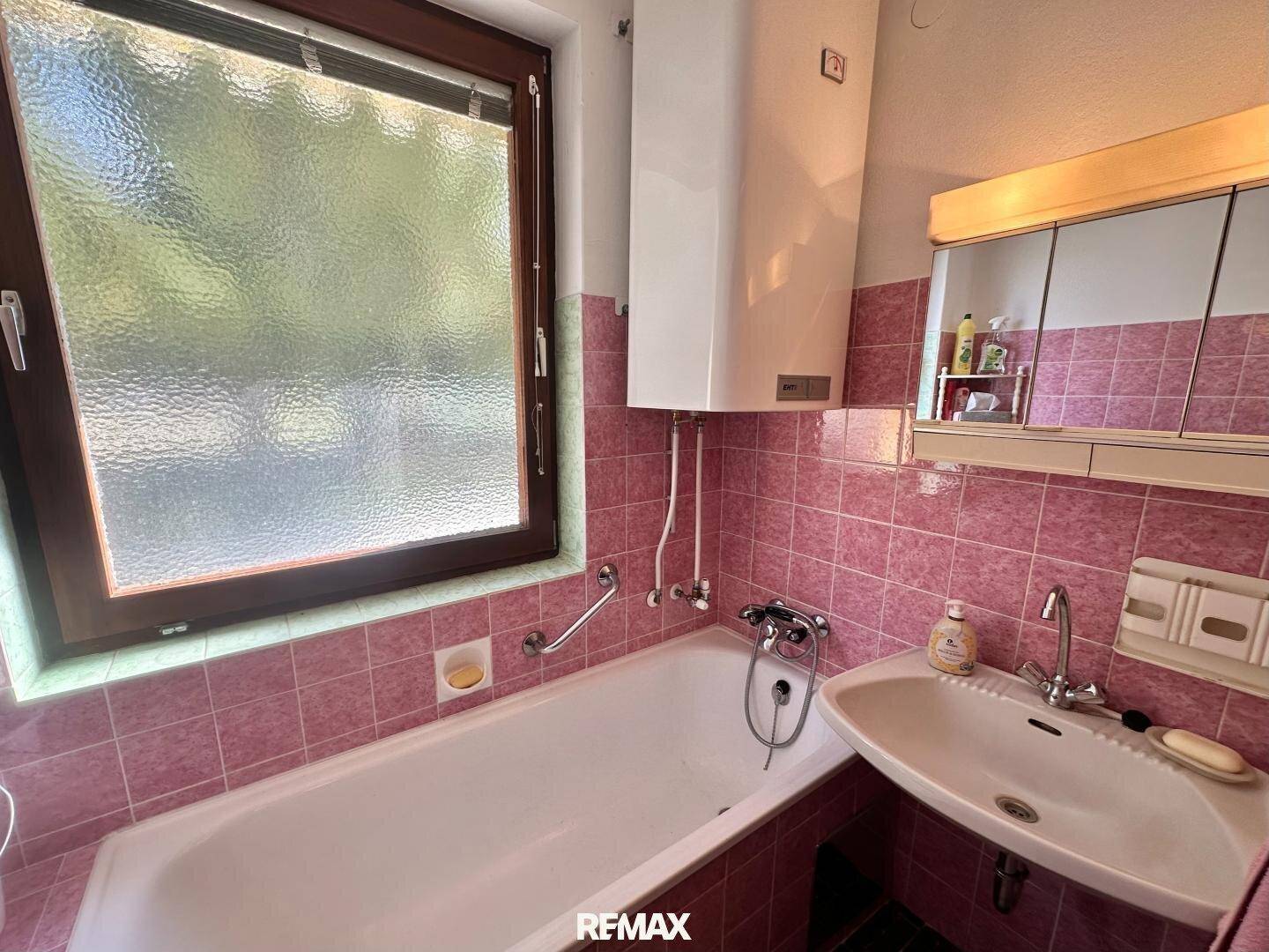 Badezimmer im Stil der 80er Jahre mit rosa Fliesen, Badewanne und Fenster.