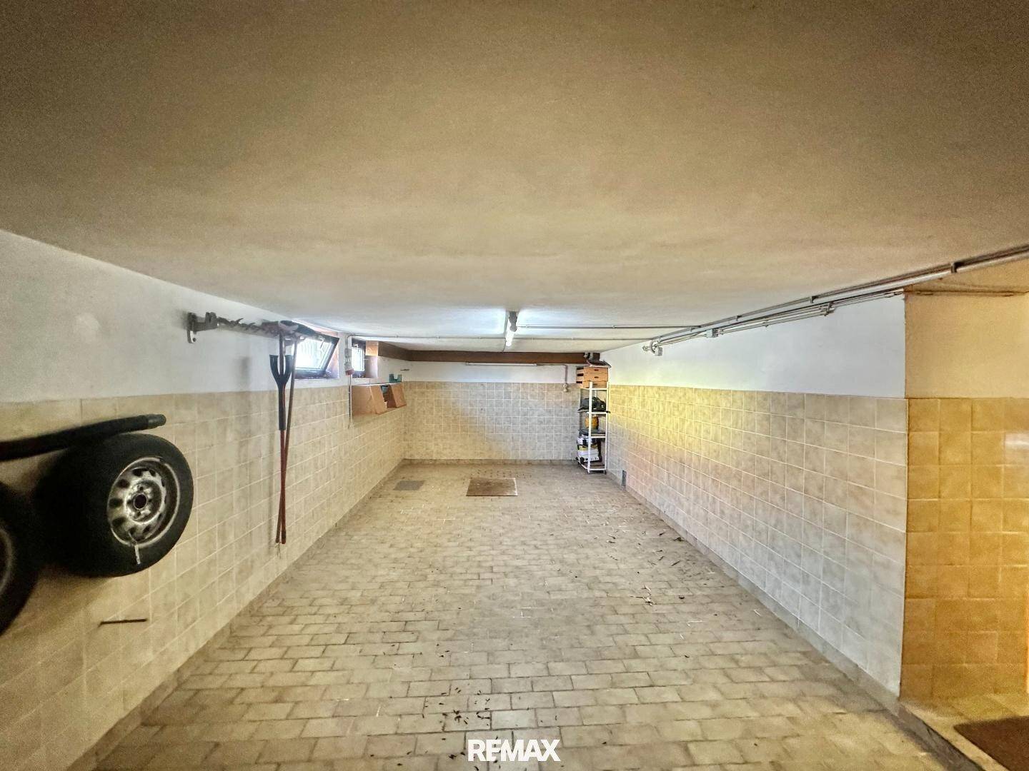 Geräumige Garage im Keller mit Fliesenboden, kleinen Fenstern und Stauraum für Reifen.