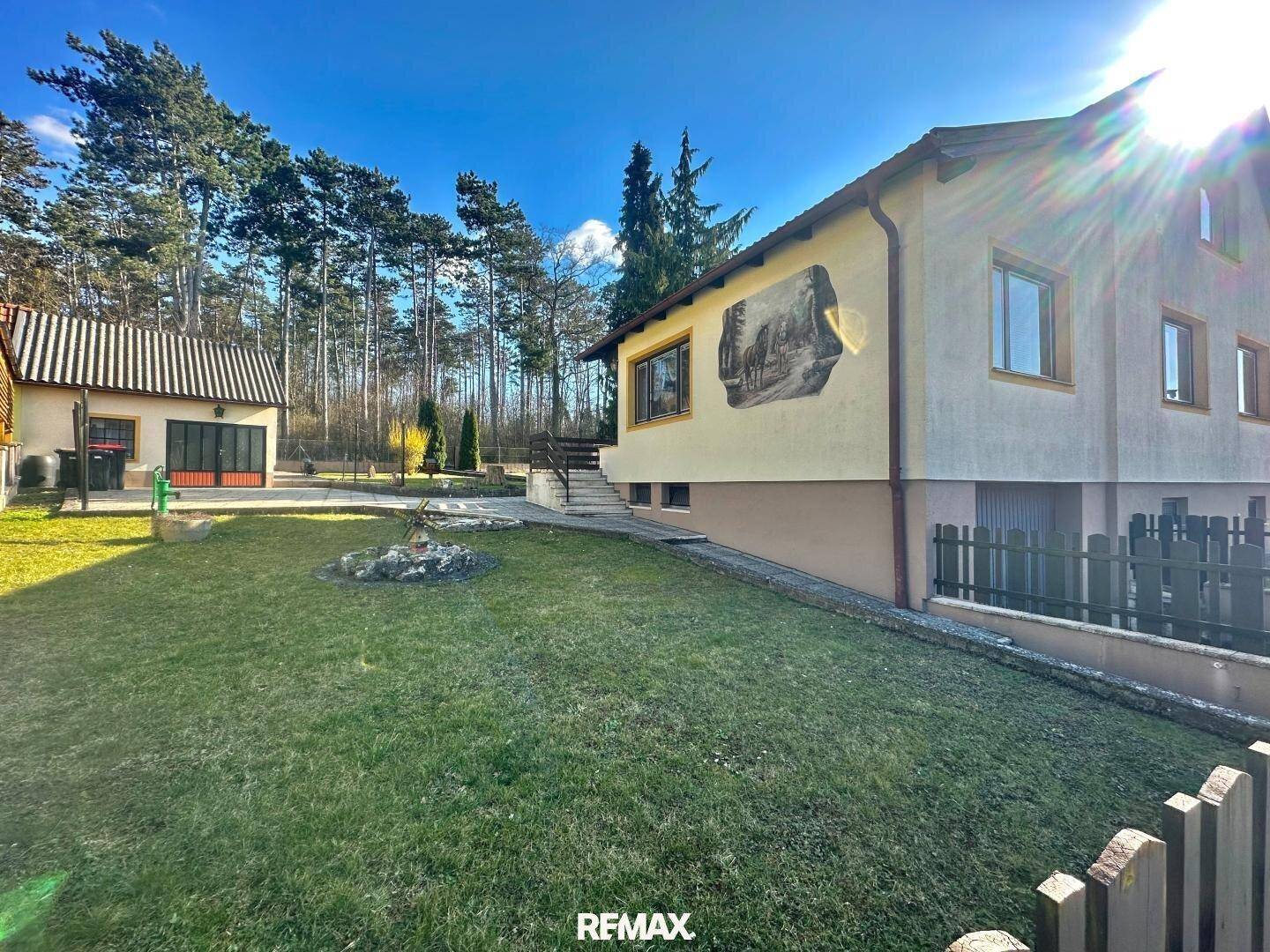 Haus mit separatem Nebengebäude, großem Rasen, Bäumen und einer Wandmalerei an der Fassade.