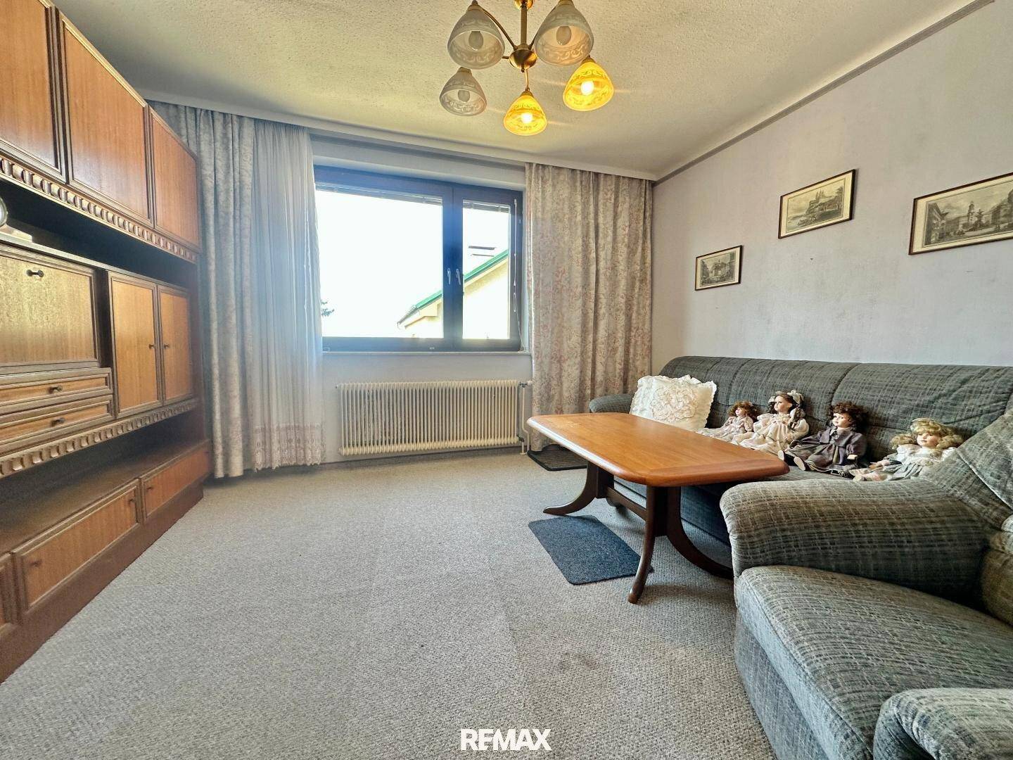 Gemütliches Wohnzimmer mit Sofa, Sessel, Teppichboden und großem Holzschrank.