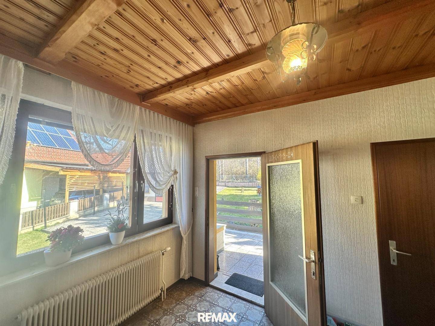 Heller Eingangsbereich mit Holzbalkendecke, Fliesenboden und Zugang zum Außenbereich.
