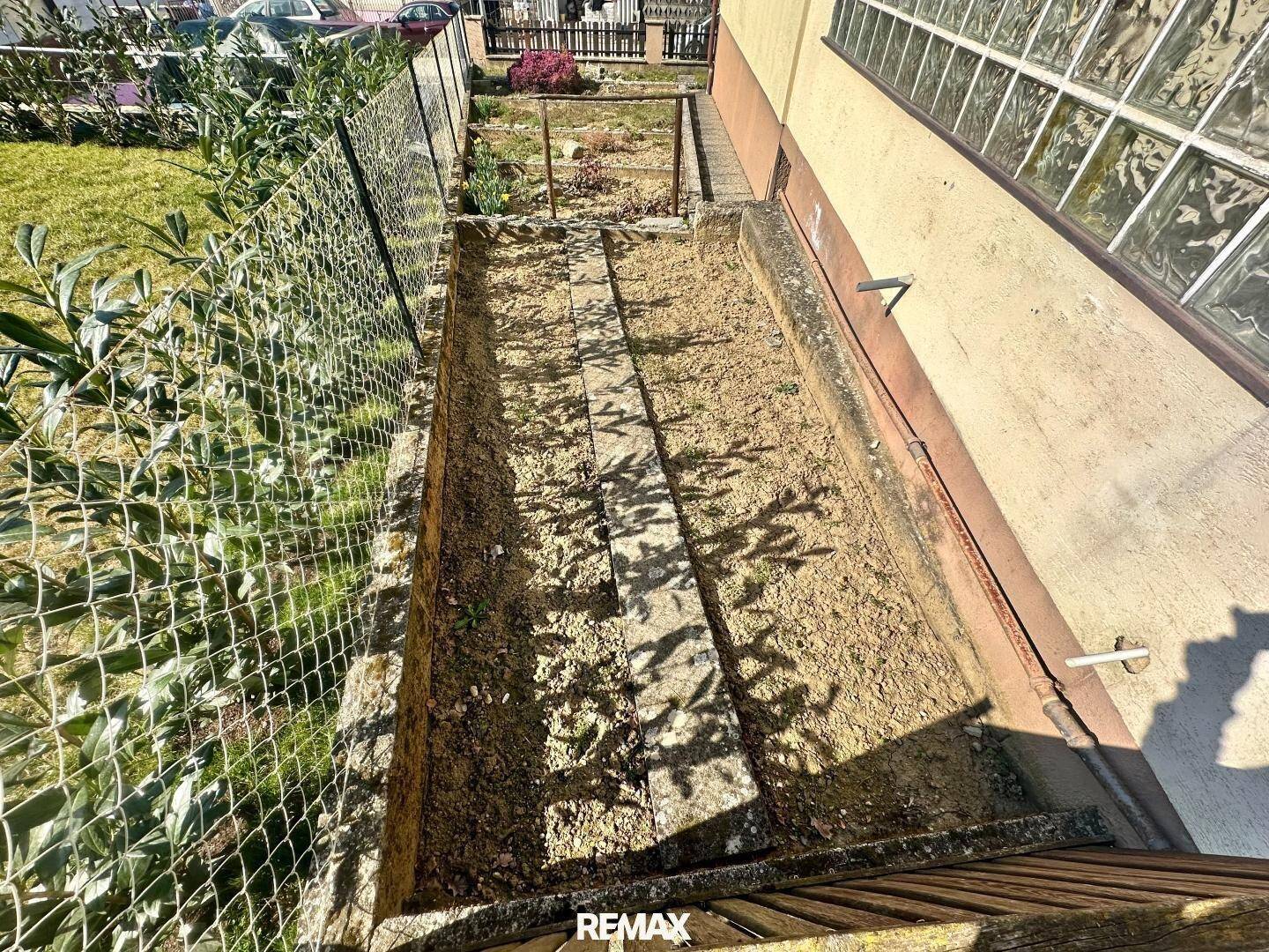 Schmaler, unbepflanzter Gartenstreifen entlang des Hauses mit Maschendrahtzaun.