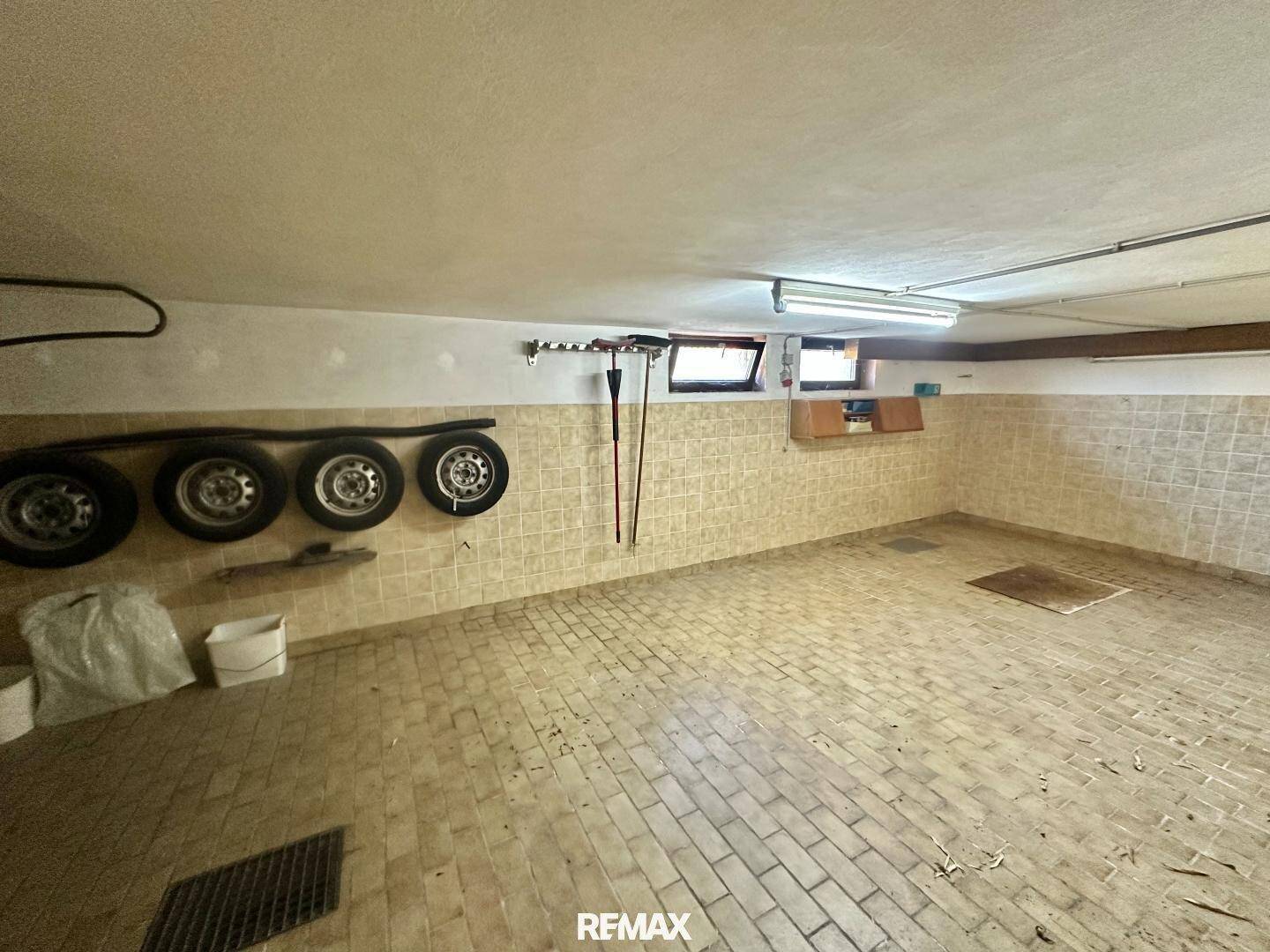Leere Kellergarage mit gefliestem Boden, kleinen Fenstern und praktischem Stauraum für Autoreifen.