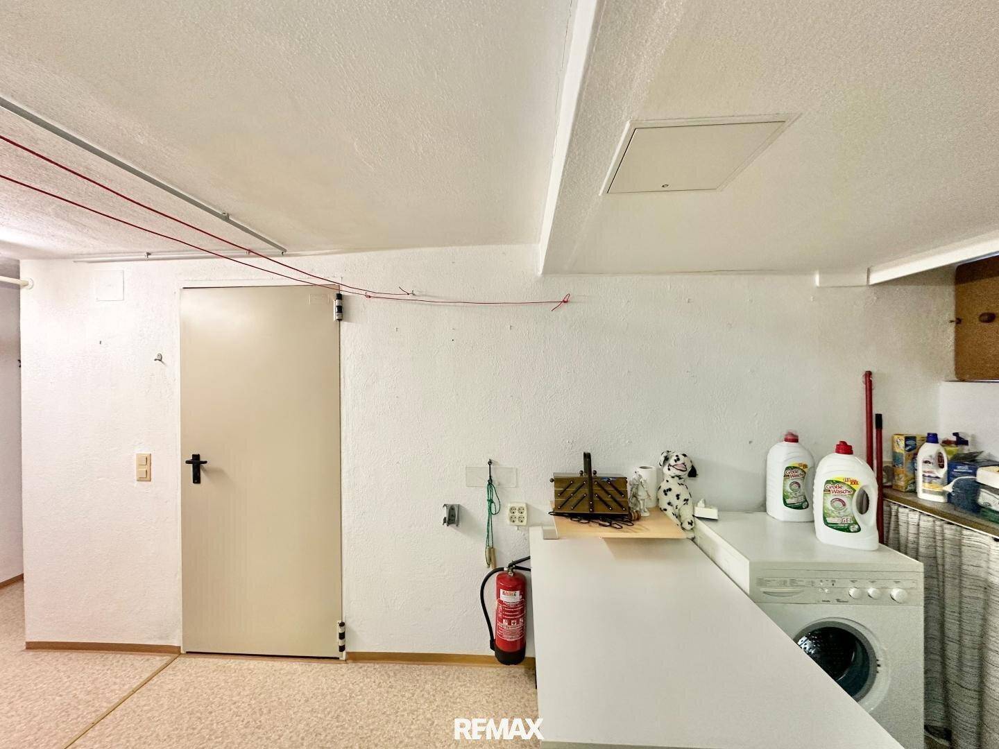 Waschküche im Keller mit Waschmaschine, Feuerlöscher und Reinigungsutensilien.