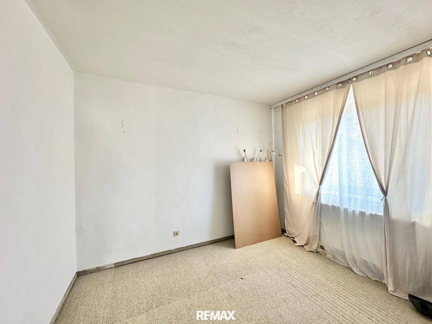 Leeres Zimmer mit Teppichboden und einem Fenster, das natürliches Licht spendet.