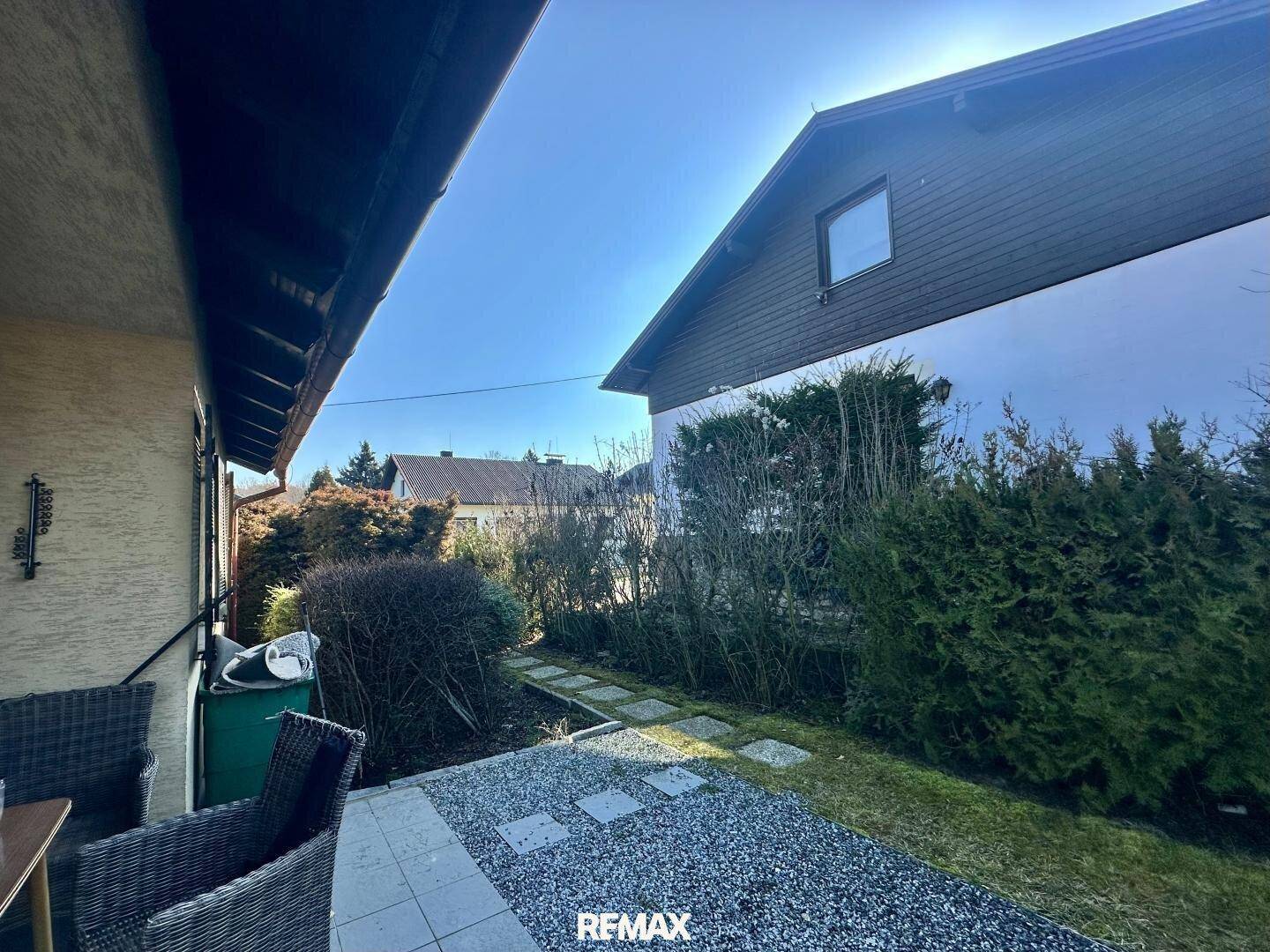 Seitenansicht des Hauses mit einem gepflasterten Bereich und einem Weg durch Hecken.