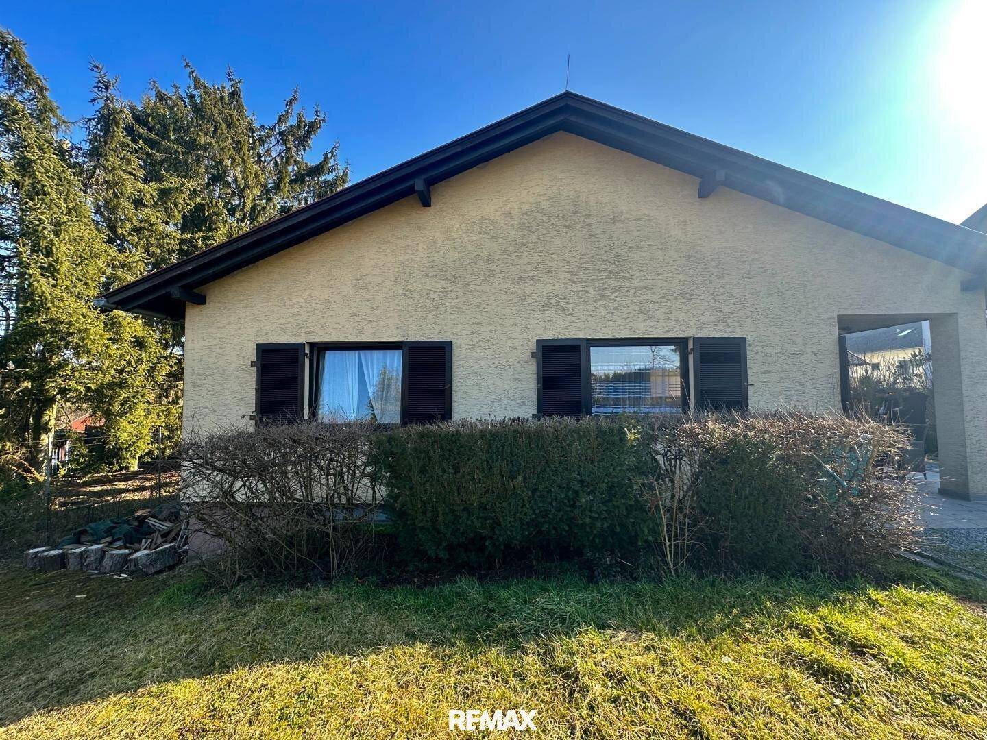 Seitenansicht des Hauses mit Fenstern, Fensterläden und gepflegten Hecken im Garten.