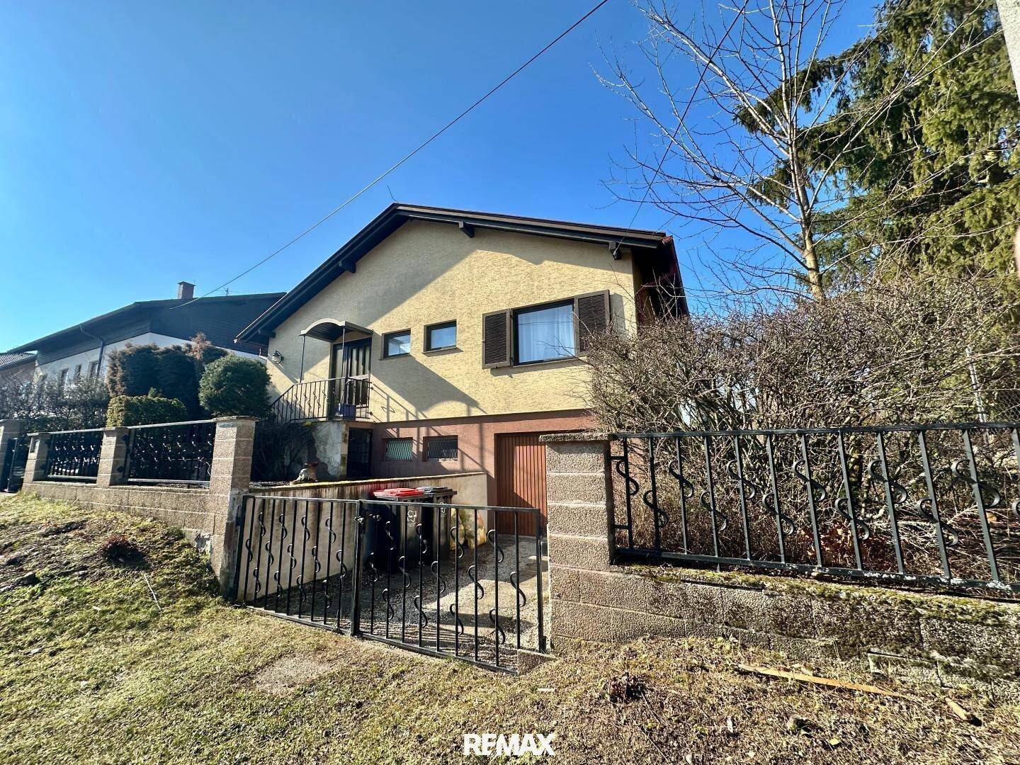 Außenansicht eines Hauses mit Garage im Untergeschoss und einem Zaun im Vordergrund.