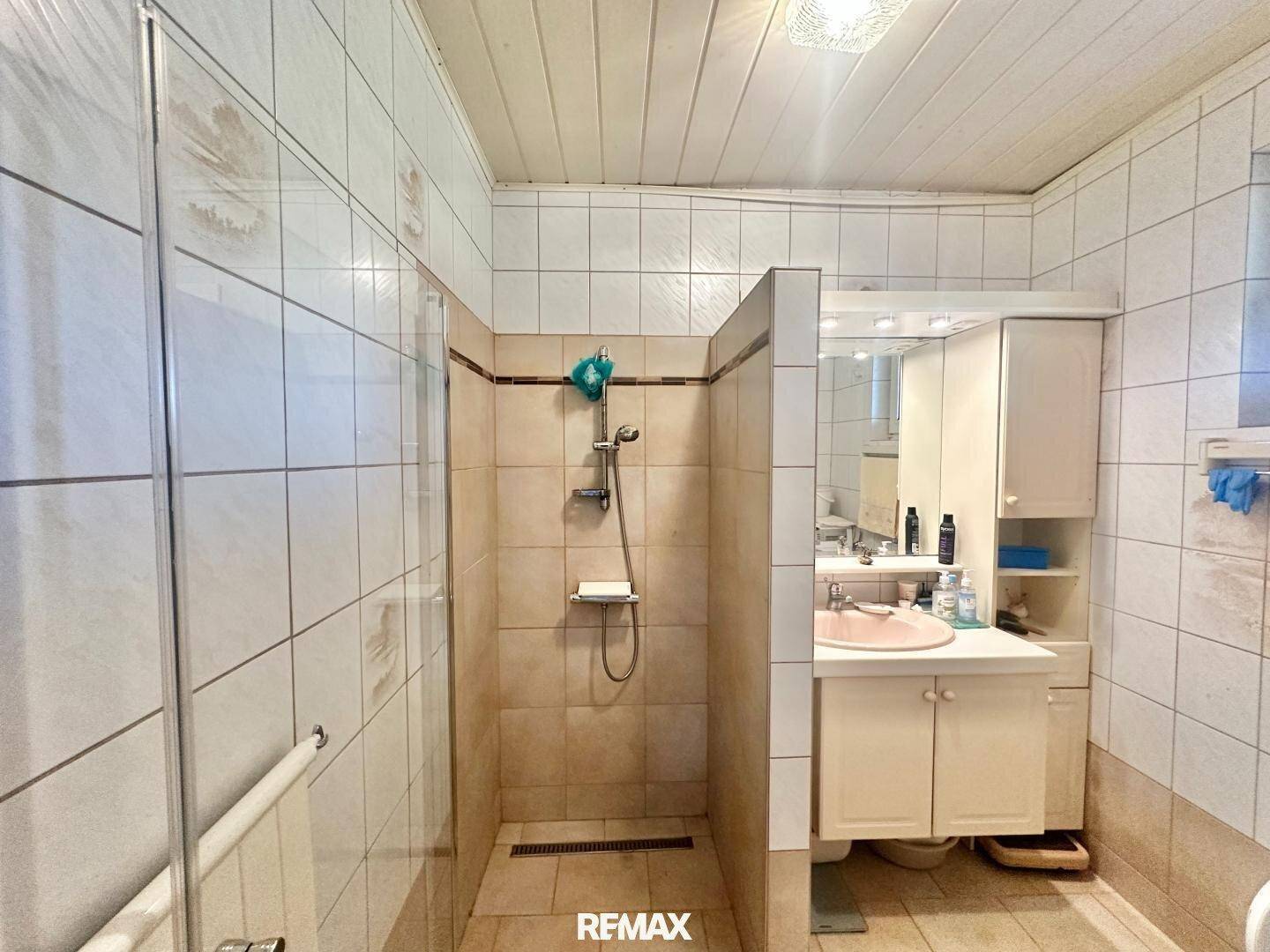 Badezimmer mit Duschkabine, Waschbecken und hellen Fliesen.