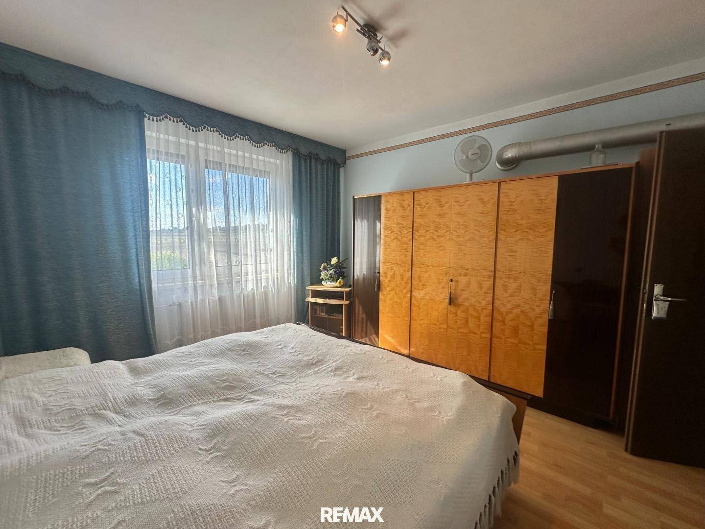 Schlafzimmer mit großem Kleiderschrank, Doppelbett und Fenster mit Vorhängen.