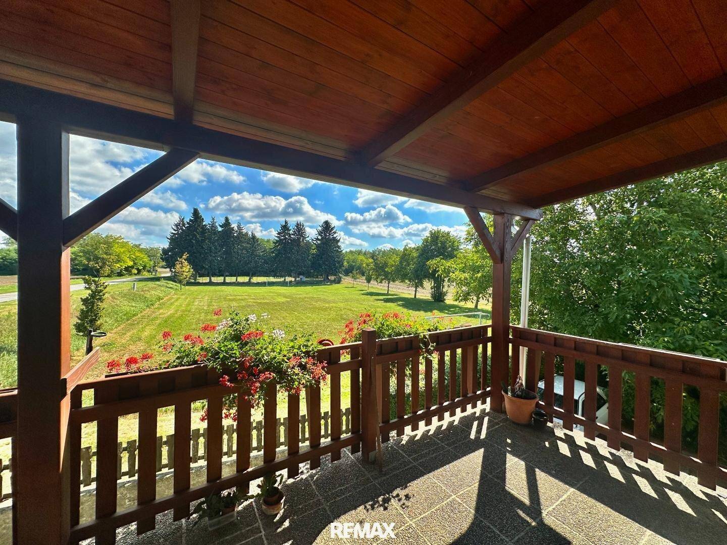 Überdachter Balkon mit Holzgeländer und Blumenkästen, der einen weiten Blick ins Grüne bietet.