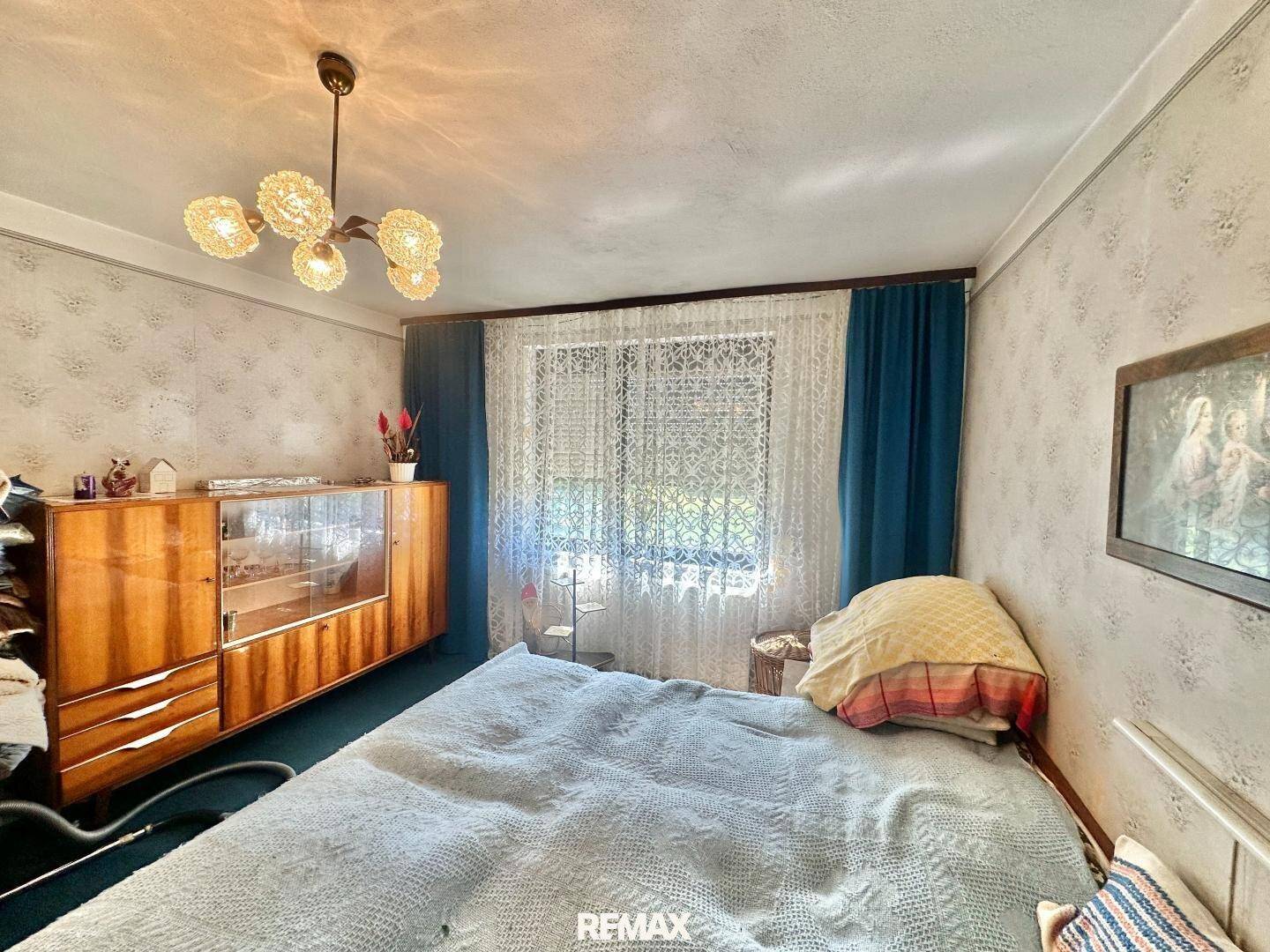 Schlafzimmer mit traditionellem Holzschrank, Doppelbett und gemusterter Tapete, die eine gemütliche Atmosphäre schafft.