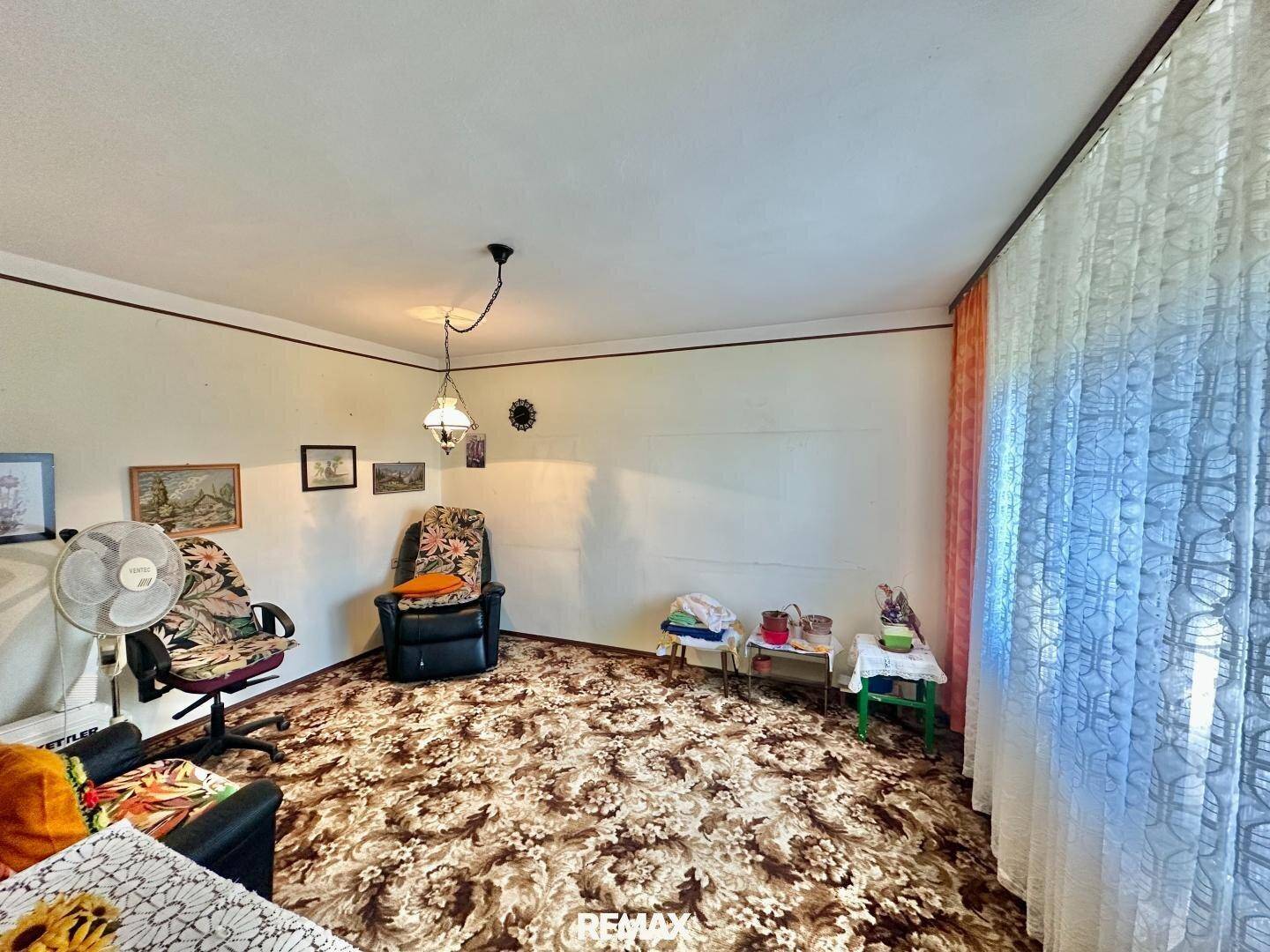 Wohnzimmer mit gemustertem Teppichboden und einem Fenster mit Vorhängen, das den Raum erhellt.
