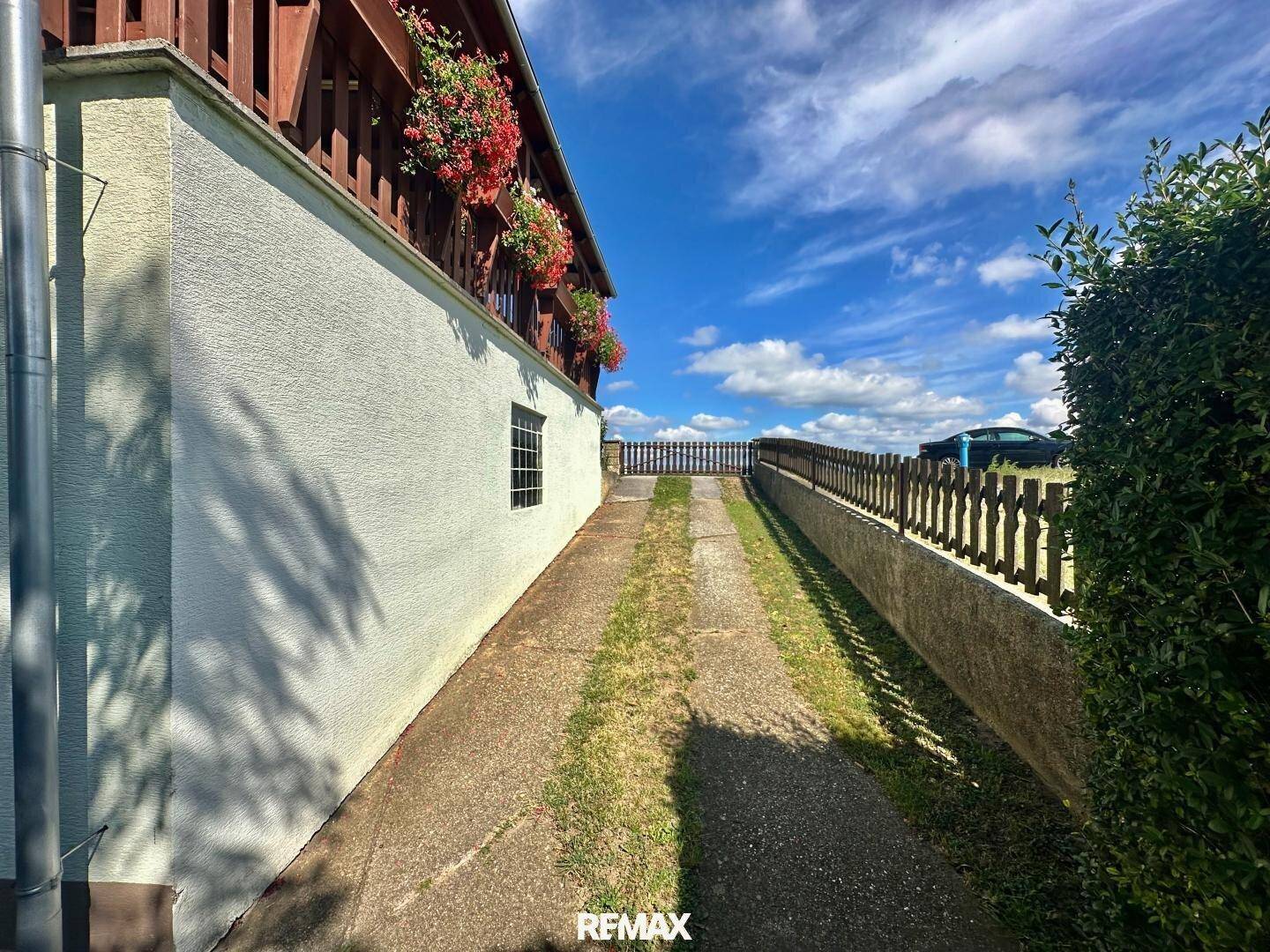 Zufahrt zum Haus mit einem Zaun und gepflegten Hecken entlang des Weges.
