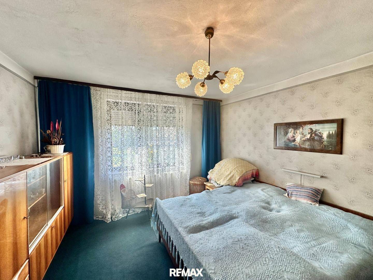 Helles Schlafzimmer mit Doppelbett, gemusterter Tapete und einem Fenster, das viel Tageslicht hereinlässt.
