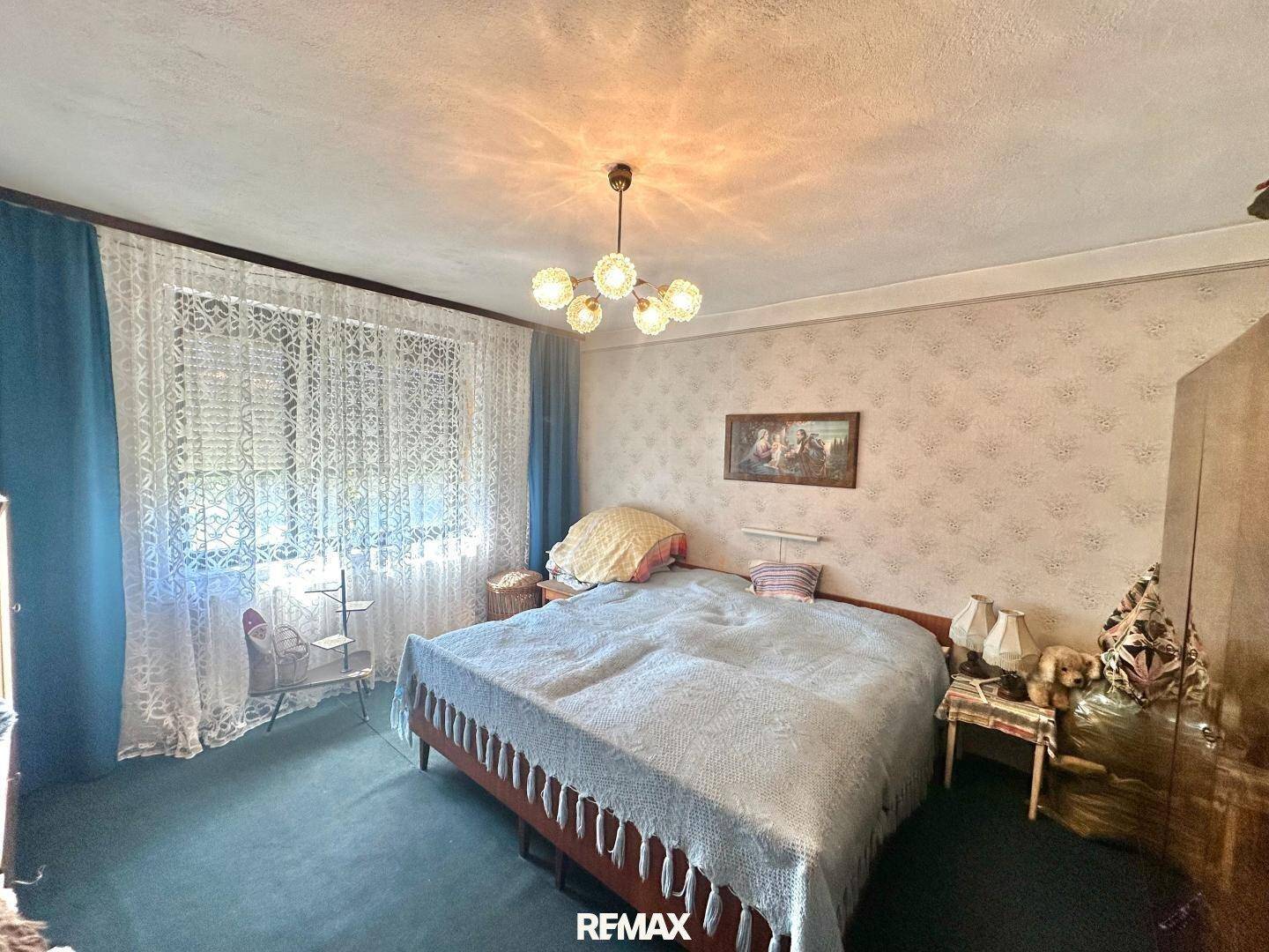 Gemütliches Schlafzimmer mit Doppelbett, gemusterter Tapete und Vorhängen, die das Fenster schmücken.