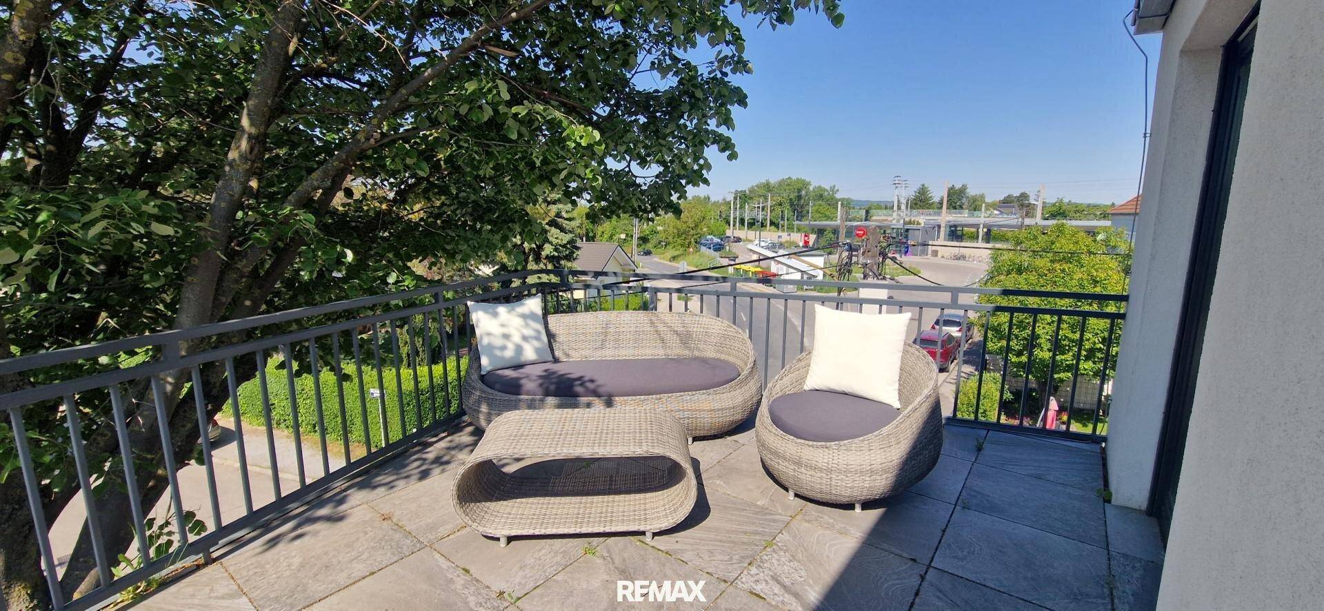 Möblierter Balkon mit Rattan-Sitzgruppe und Blick ins Grüne an einem sonnigen Tag.