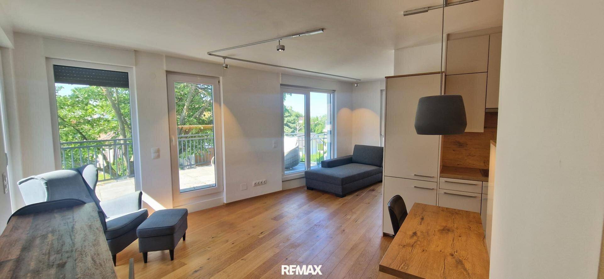 Helles Wohnzimmer mit Holzboden, großen Fenstern und Zugang zu einem Balkon.