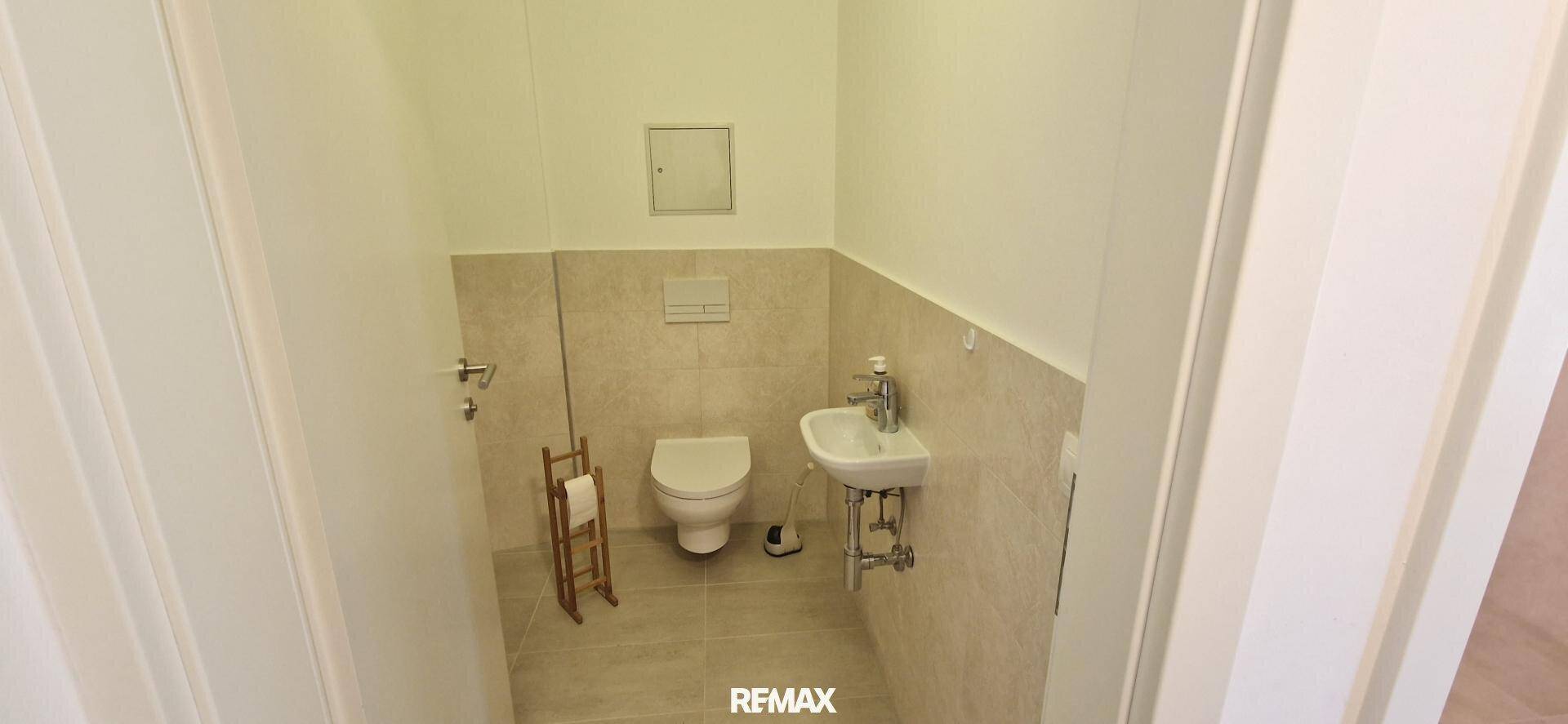 Kleines Gäste-WC mit Wand-WC, Waschbecken und hellen Fliesen.