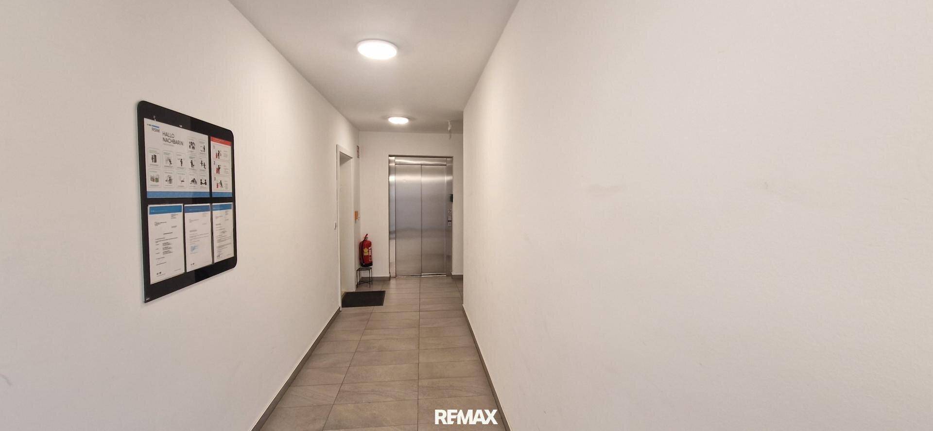 Heller Flur im Gebäude mit Fliesenboden und einem modernen Aufzug.